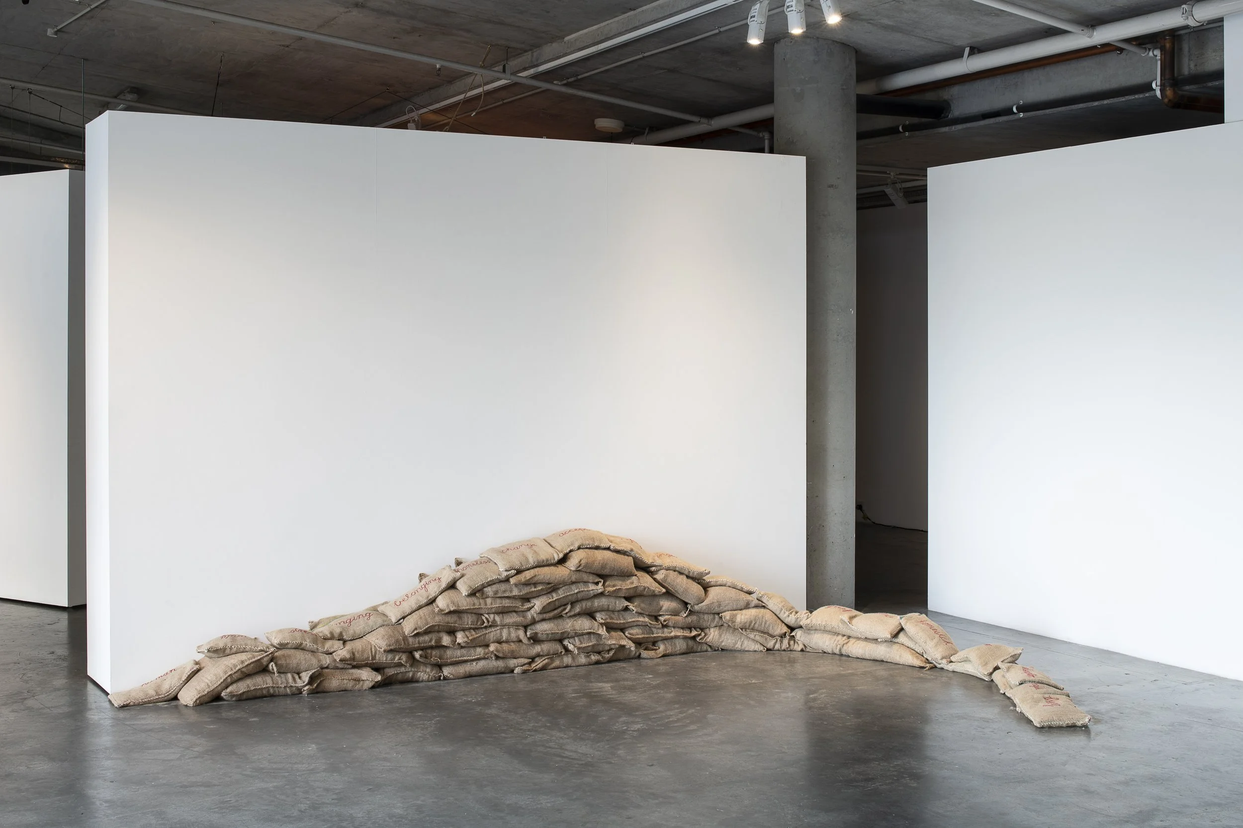 A pile of sandbags in a line against a wall of the gallery.