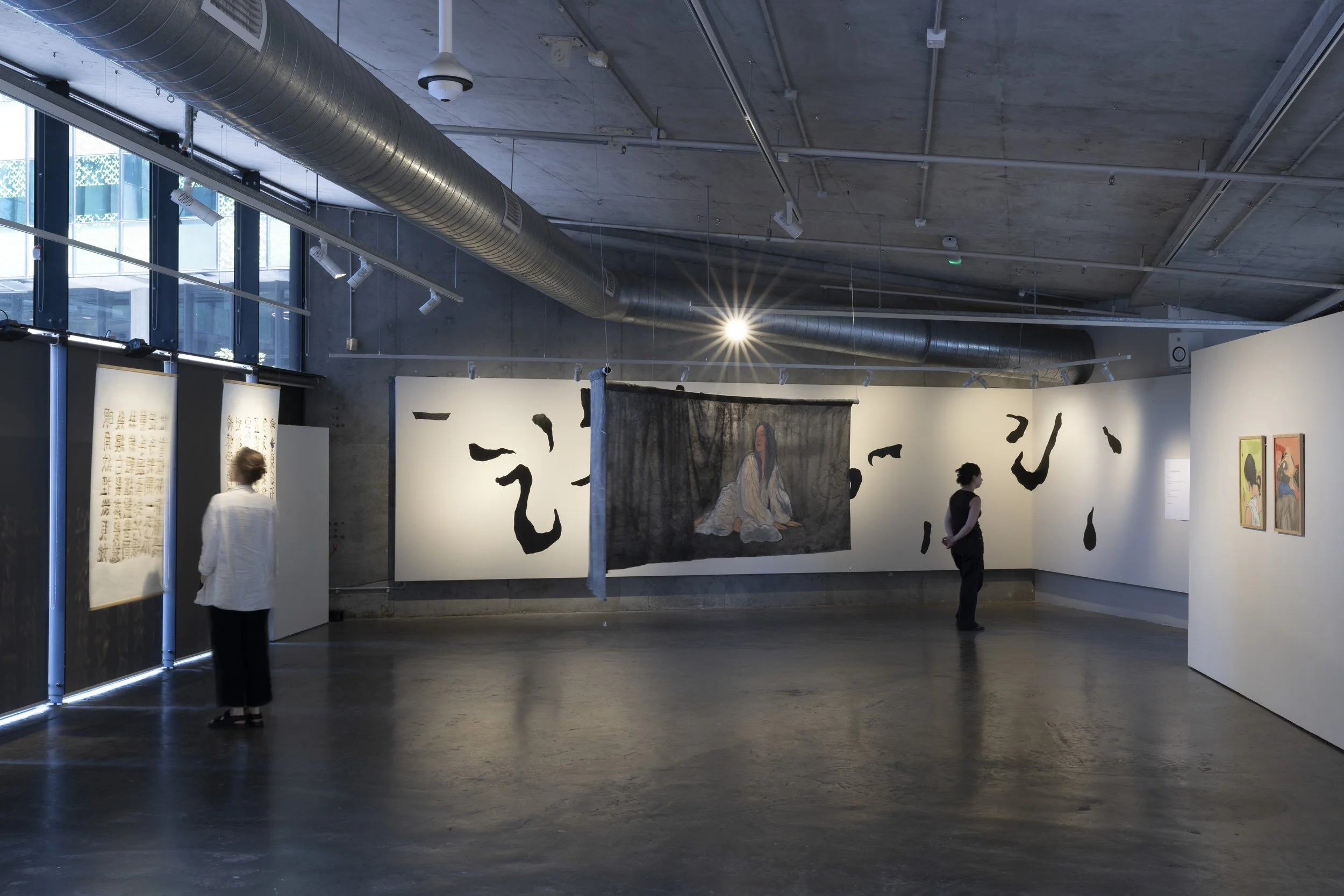 Left to right. 2 hanging papers with calligraphy burn marks. Hanging silk of figure in white lying on black. Mural of fragmented black strokes on white wall. 2 watercolour portraits of braiding on green & red backgrounds.