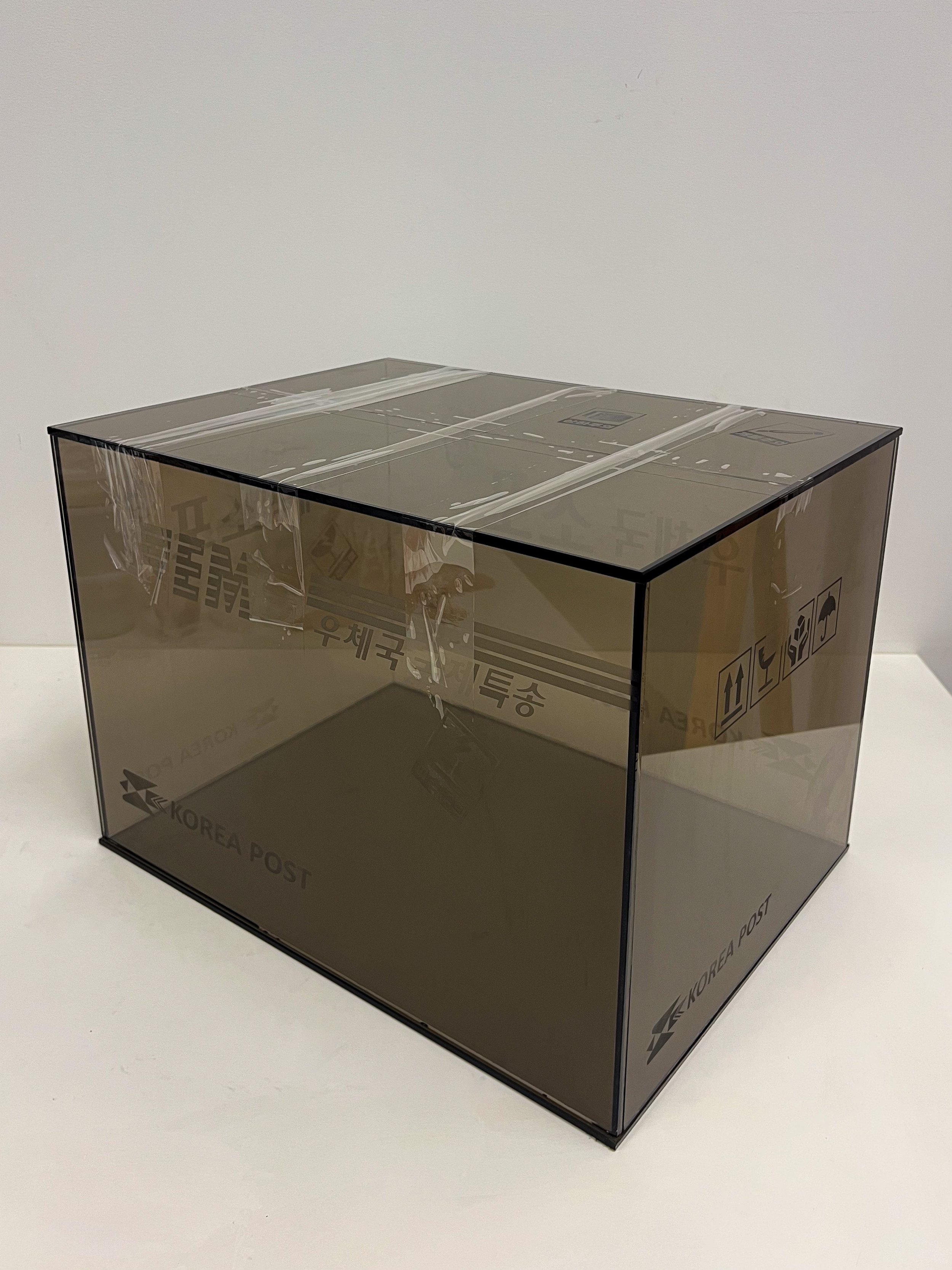 Estelle Yoon, 우체국 소포 (Post Office Parcel), 2026. Sculpture of a parcel with Korea Post branding made from brown, translucent glass, held together with clear packing tape.