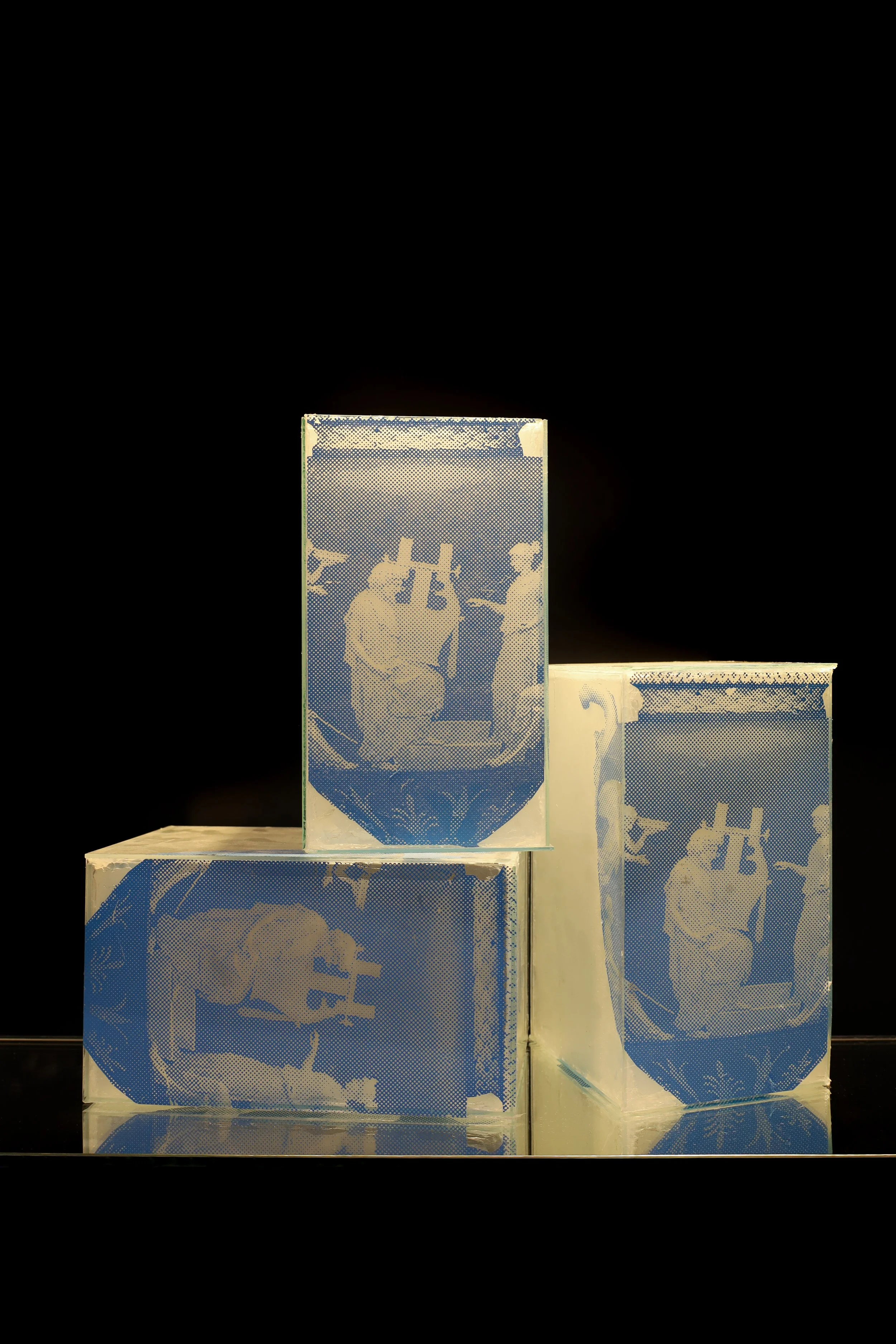 3 glass rectangle boxes with one on its side and one stacked on top. Printed in blue on the glass is images of ancient Greek or Roman style vases, depicting figures holding instruments.