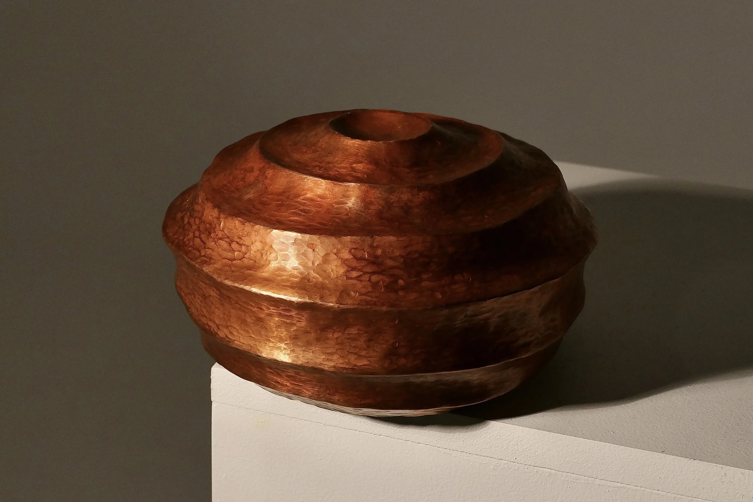 Phoebe Webb, Formal matters, 2026. Round copper sculpture with layers horizontal The surface is a deep, rich orange with stippled surface texture.
