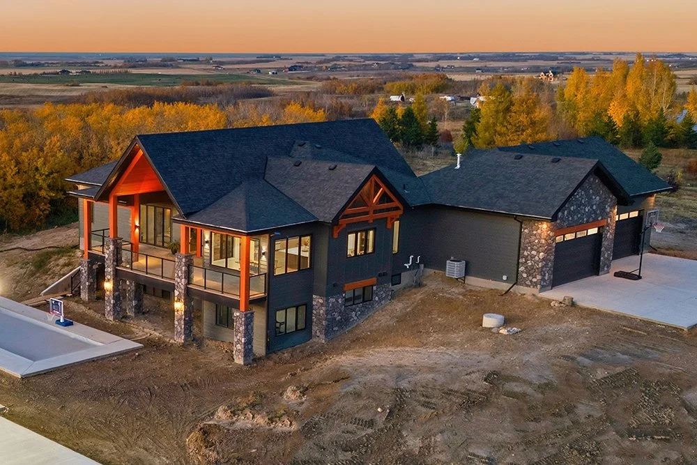 A real twilight photo of a new home: single-story brick house with three-car garage, landscaped yard, and a sunset sky in the background.