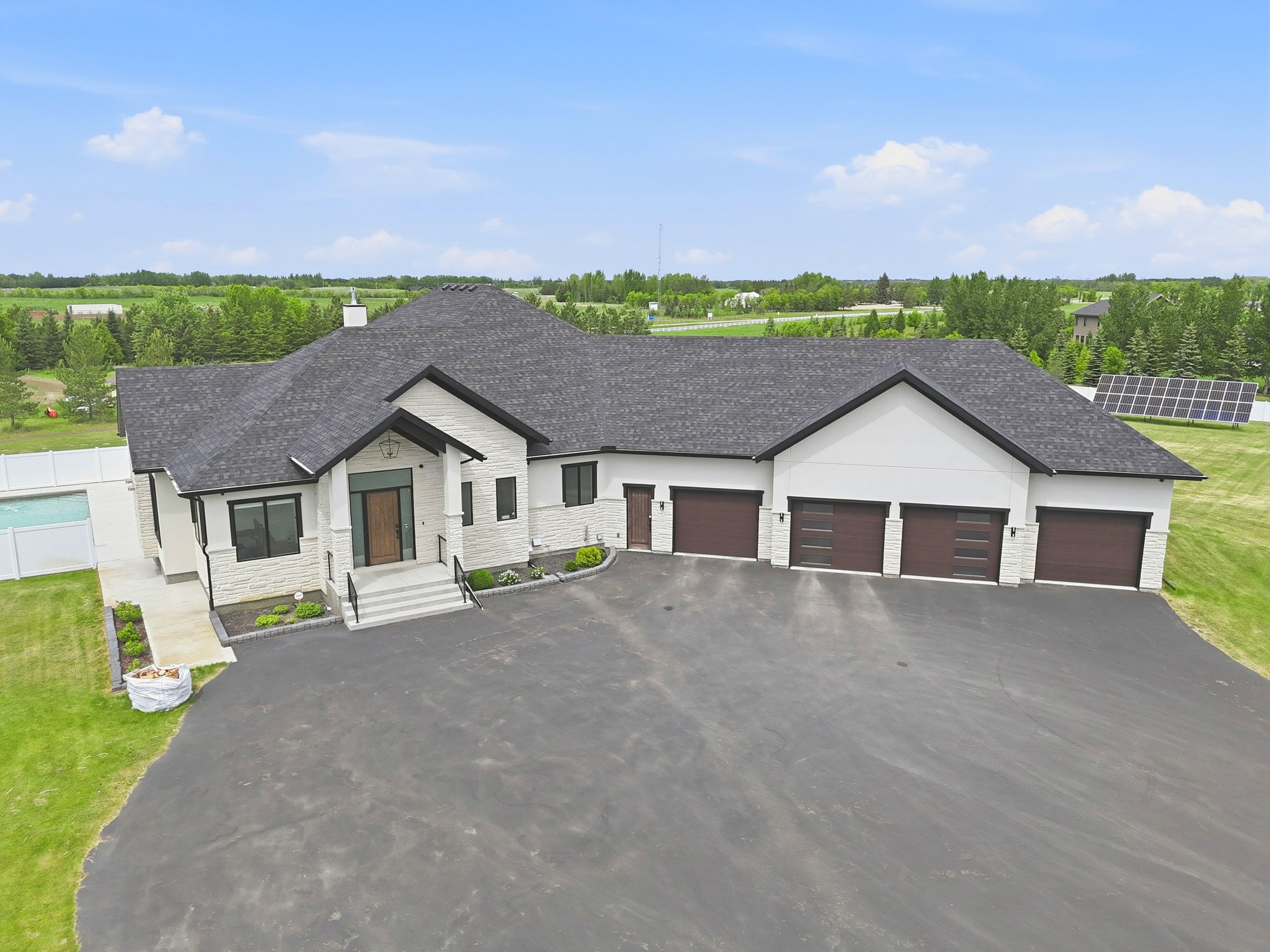 Modern single-story house with black roof, four-car garage, and large driveway, captured through stunning drone photography.