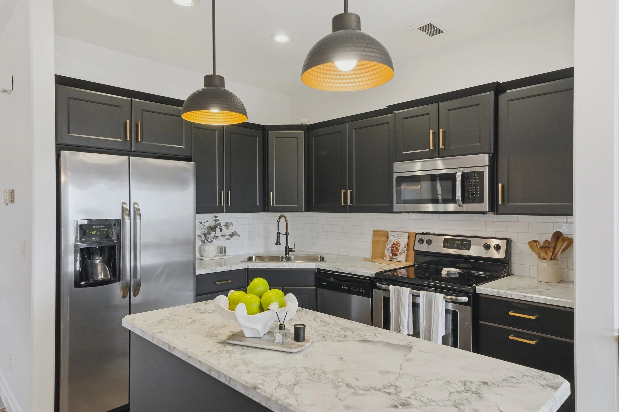 Modern kitchen with black cabinets, marble countertops, stainless steel appliances, and two pendant lights over a central island.