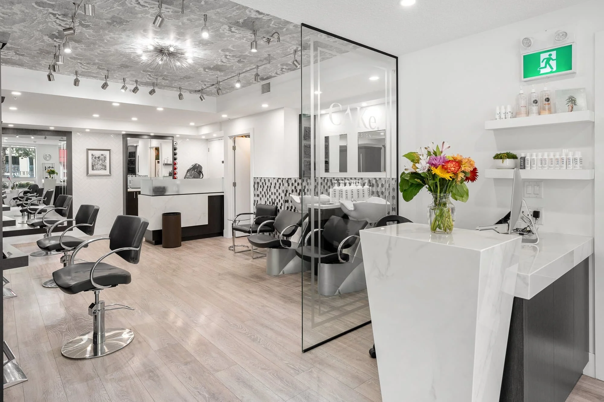 Modern, bright hair salon featuring stylish commercial interiors with black chairs, large mirrors, and a white marble reception desk.