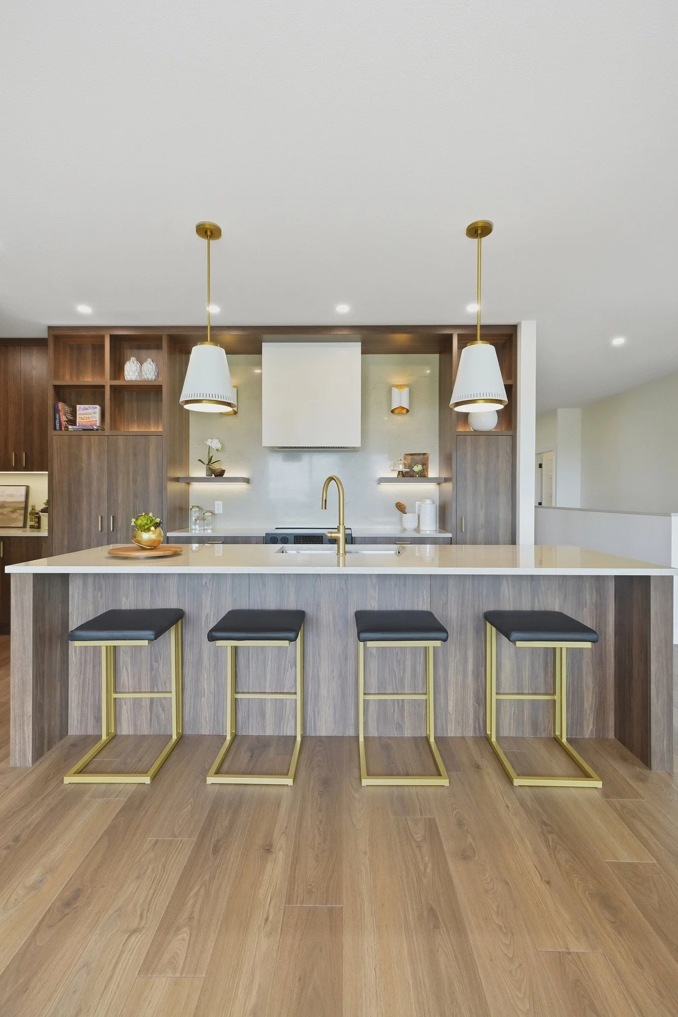 Modern kitchen with a wood island, four black barstools, gold accents, pendant lights, and open shelving.