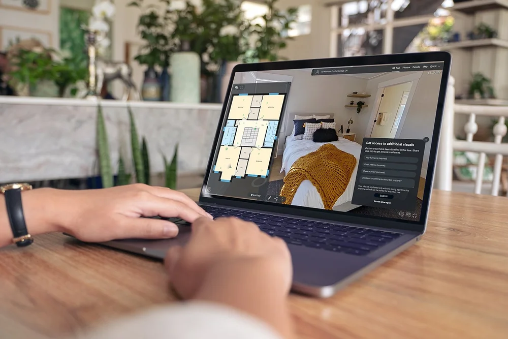 A person uses a laptop to explore a virtual property tour with a floor plan and room view