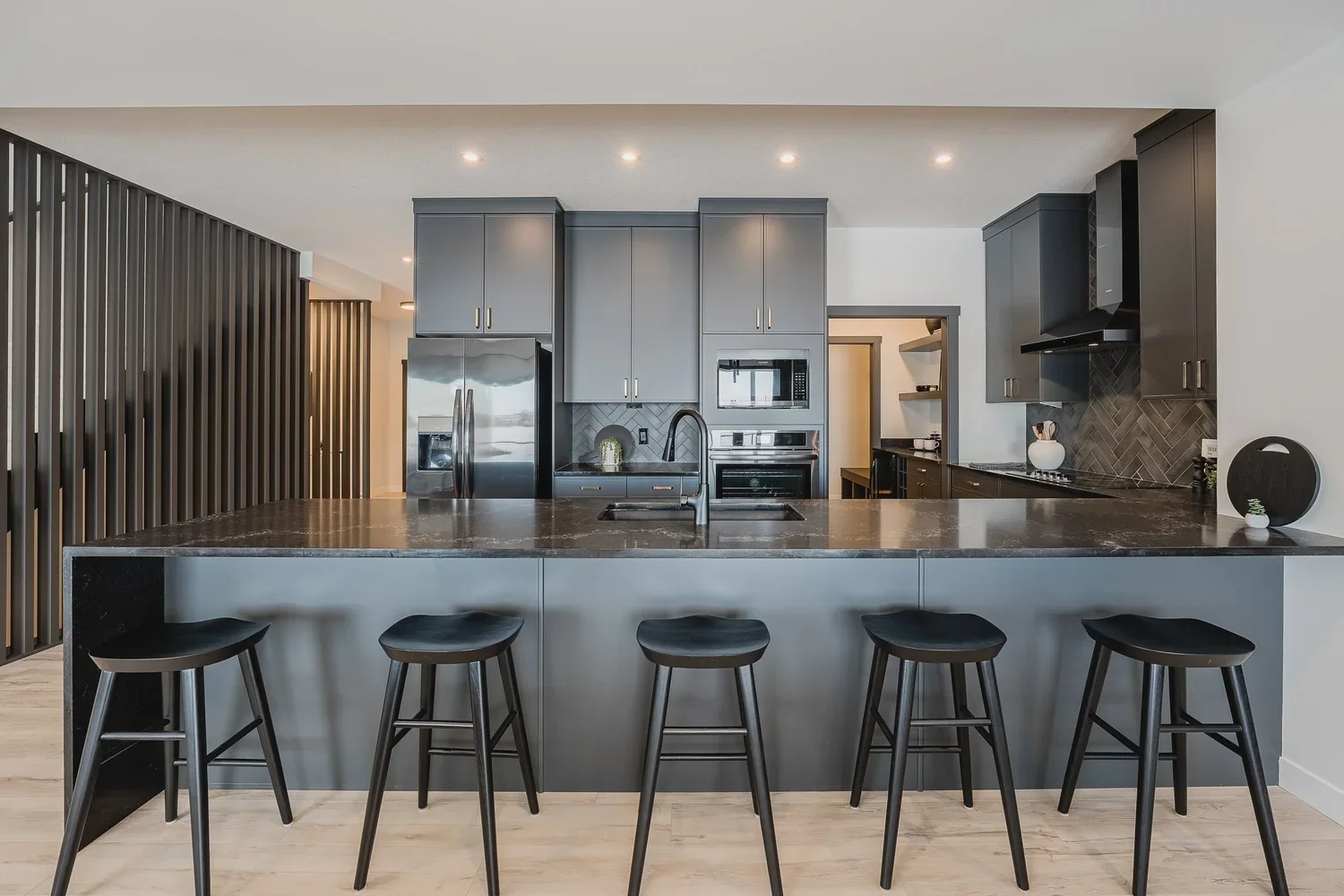 Modern kitchen with dark wood cabinets, black appliances and quartz island lit by pendant lights.