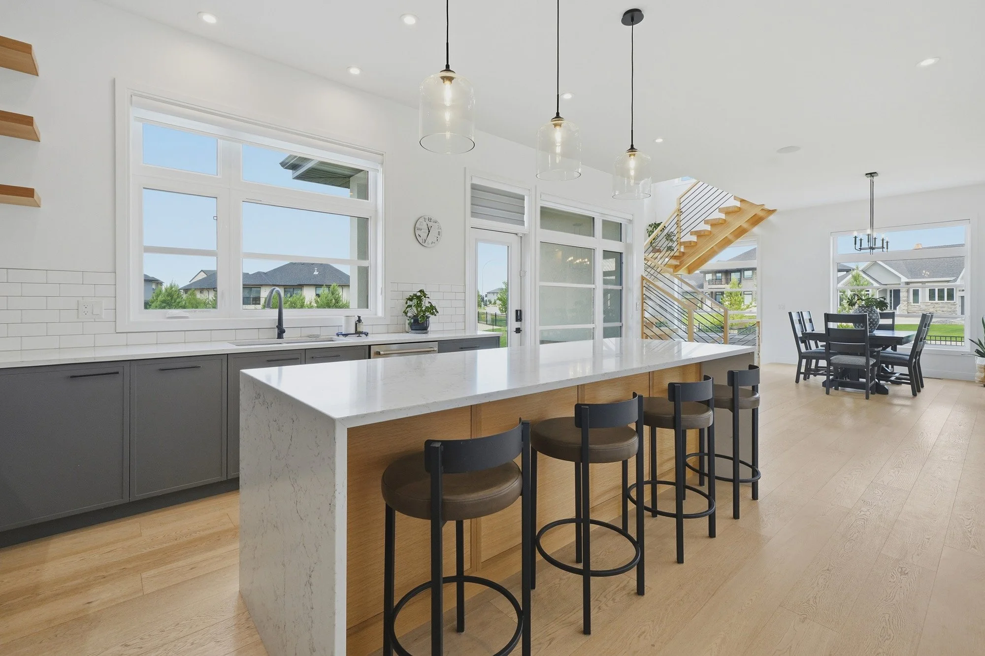 Open-concept kitchen with a long waterfall island, black stools and large windows providing abundant natural light