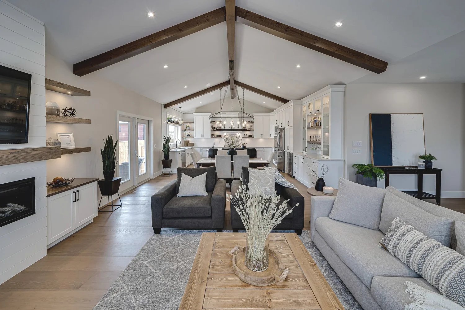 Bright open-concept living room and white kitchen with vaulted ceiling and exposed wood beams.