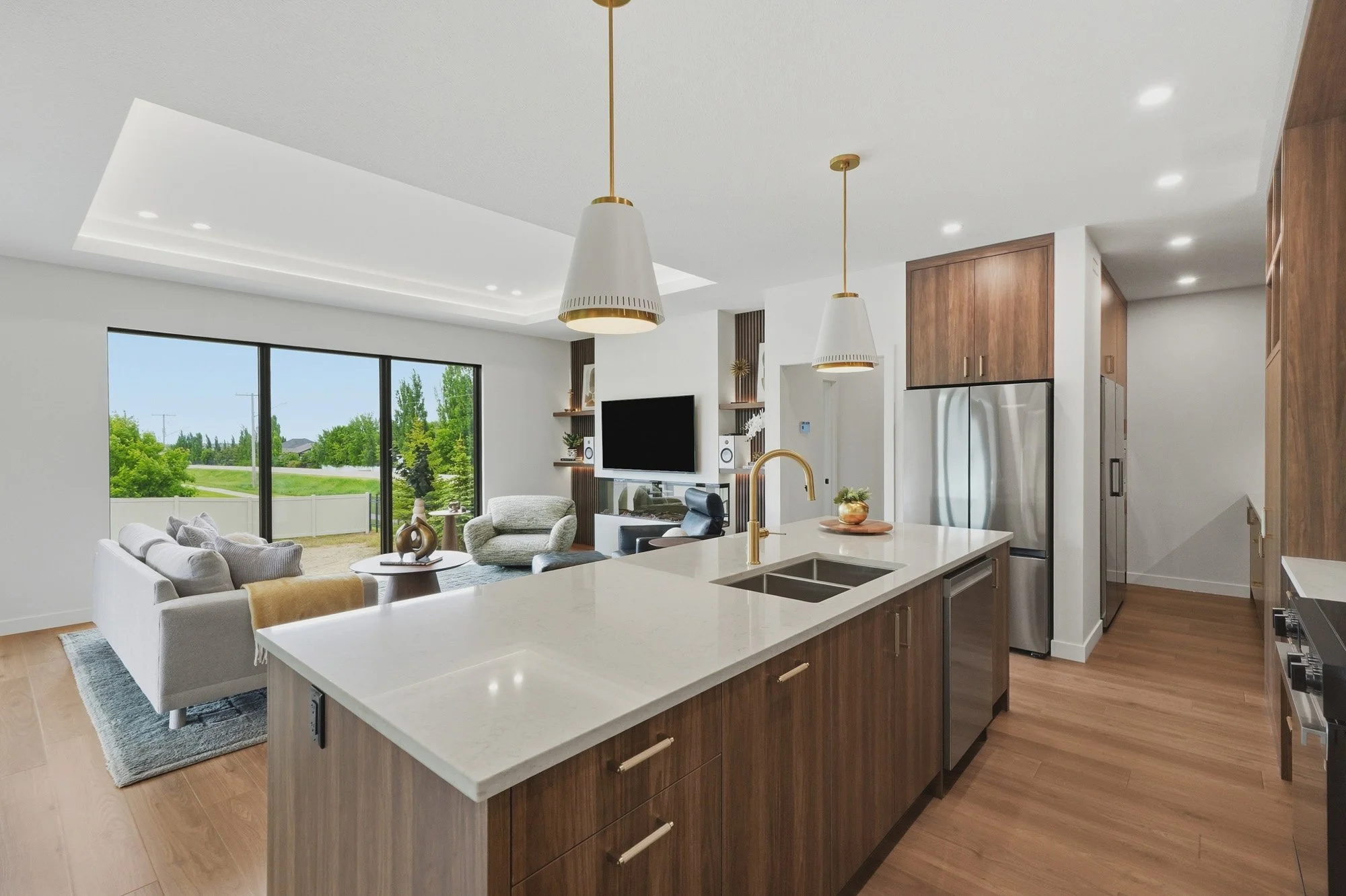 Modern open-concept kitchen and living room with wood accents, white countertops, and large window showing greenery outside.