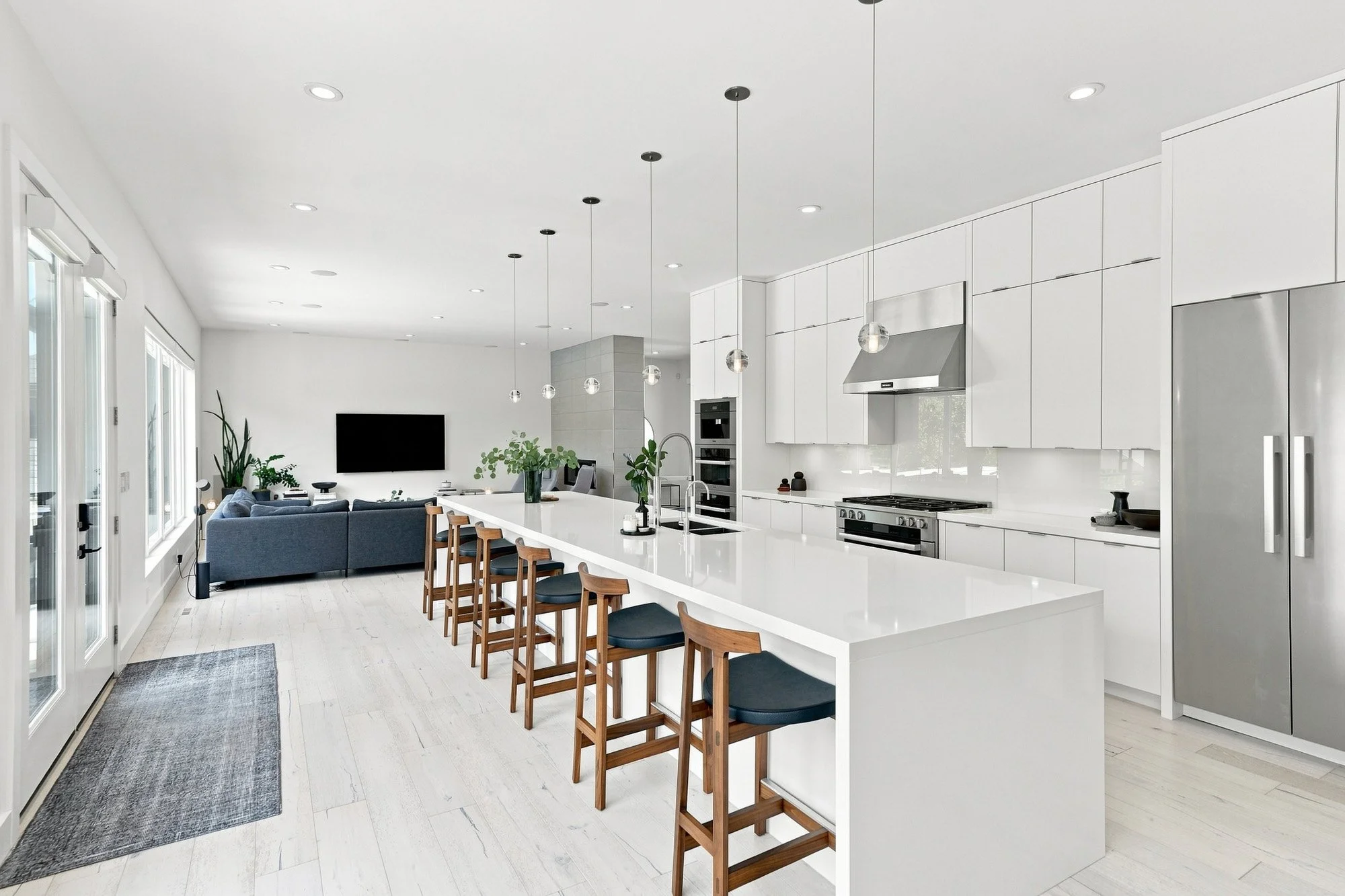 Bright modern kitchen with white cabinets, island seating, pendant lights, and open living space in the background.