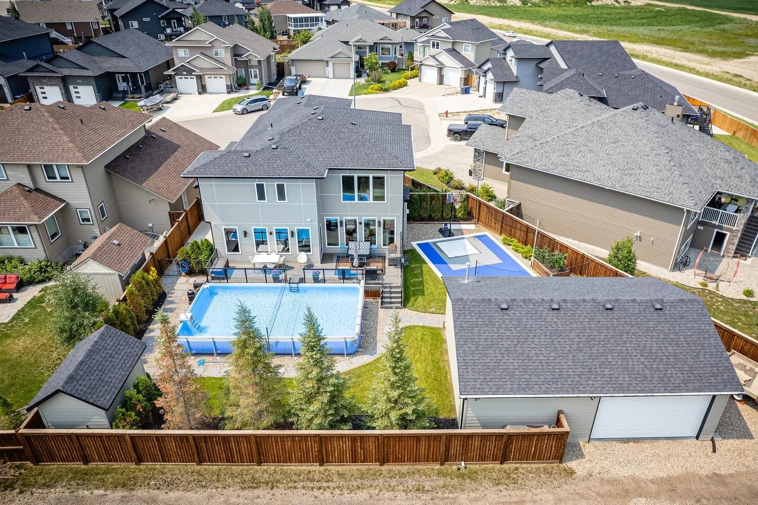 Aerial view of a large pie-shaped backyard with pool, basketball court and detached garage.