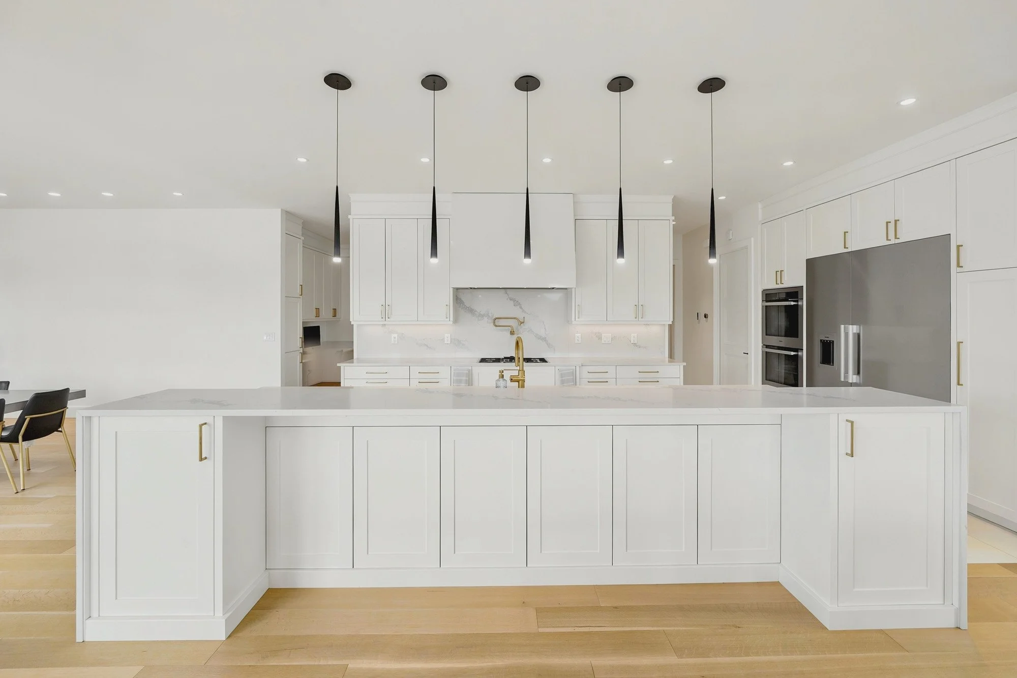 Bright white kitchen with an oversized island, minimalist pendant lights and warm wood flooring.