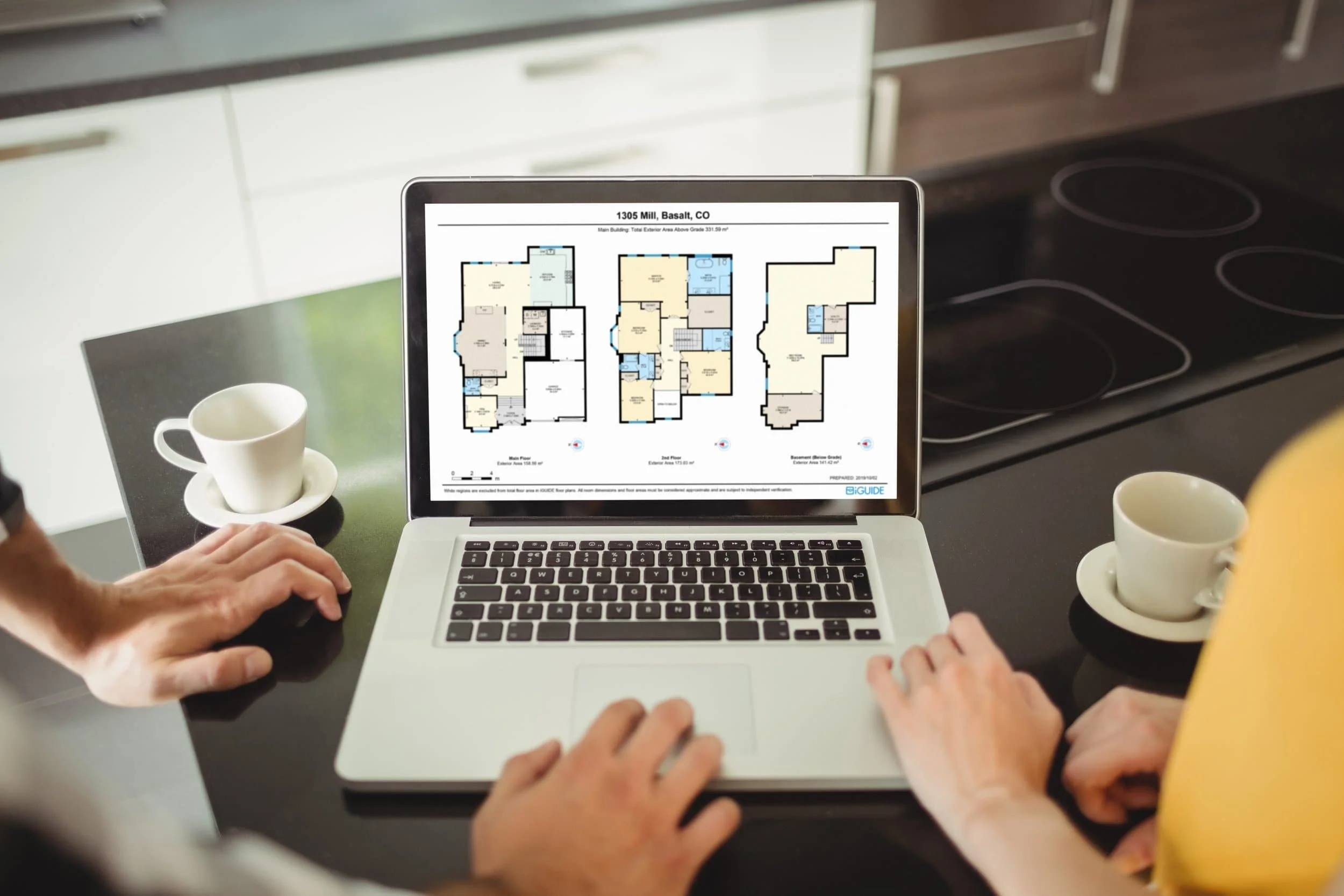 Two people explore a digital floor plan with virtual tours on a laptop at the kitchen counter, coffee cups nearby.