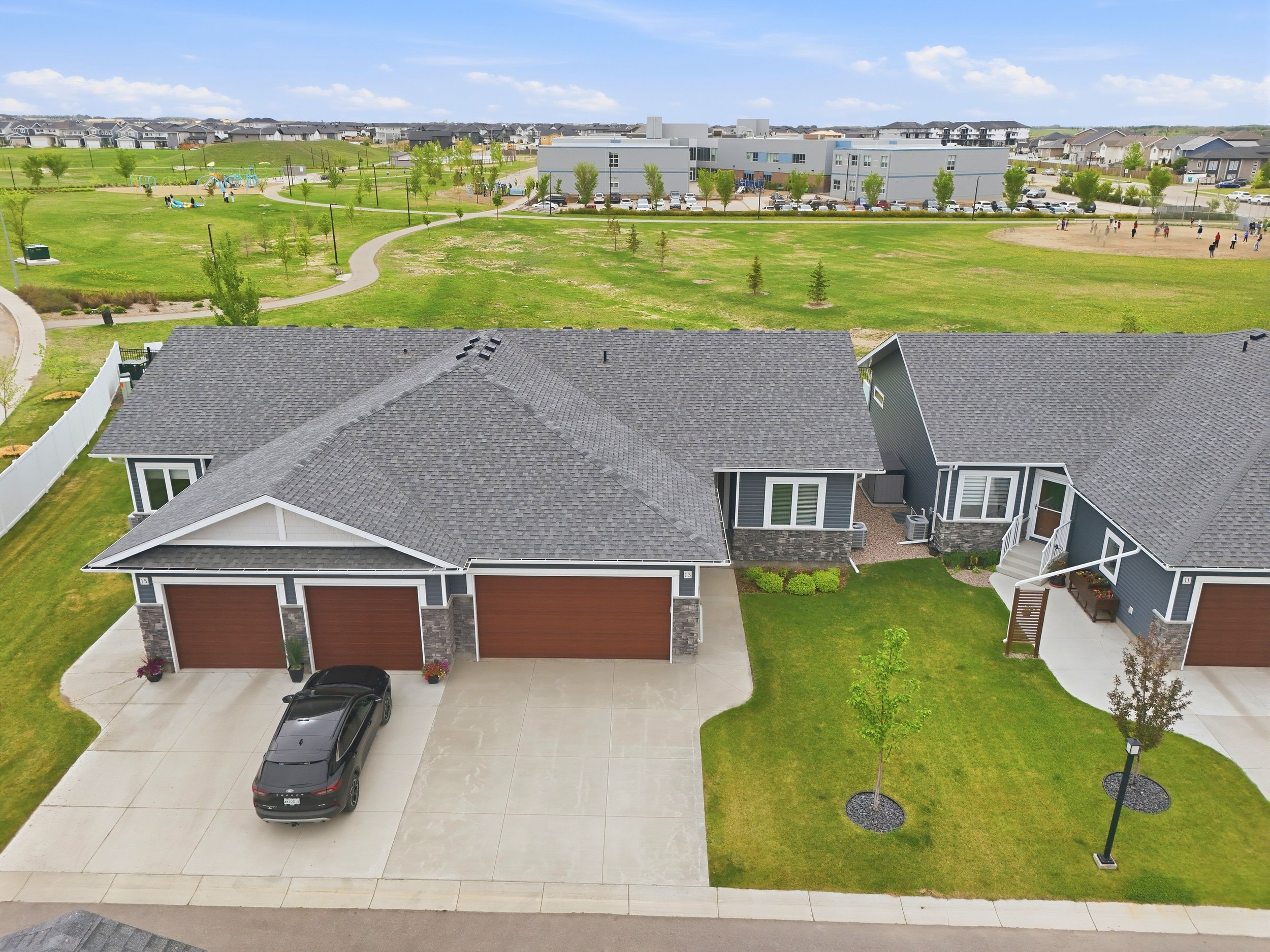 Real estate drone photography in Saskatoon showcasing a modern home, landscaped yard, and nearby park and school views.