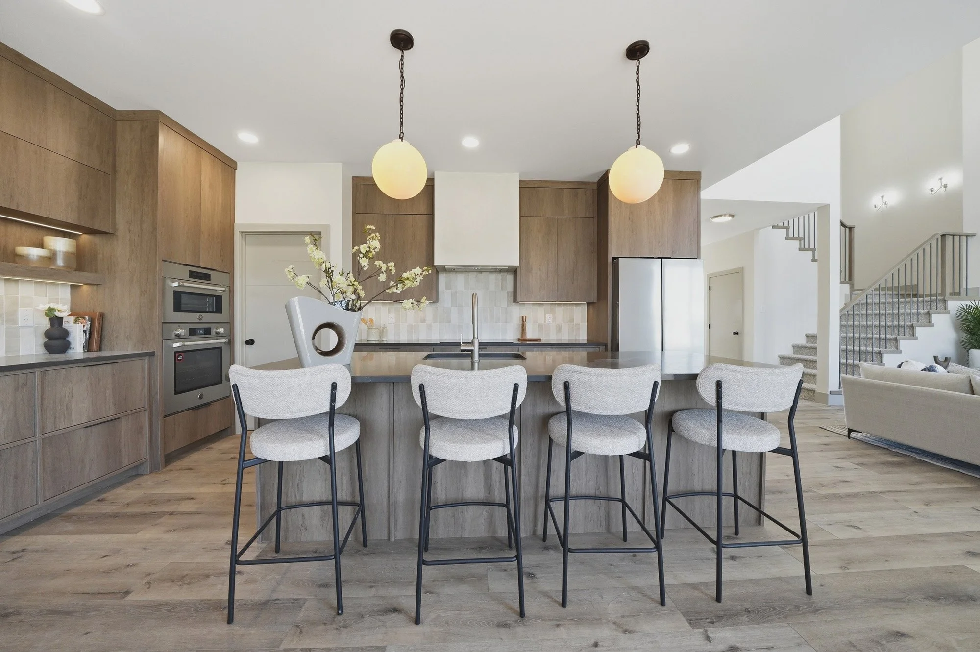 Modern kitchen featuring warm wood cabinetry, globe pendant lights and seating for five at the island