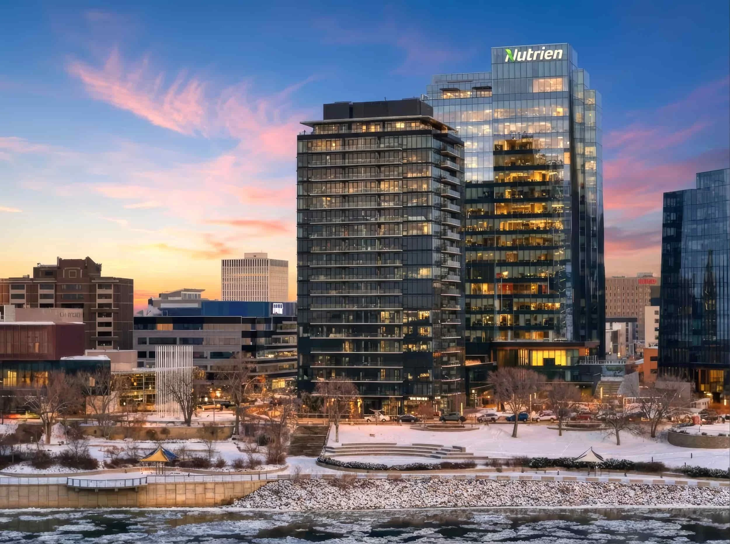 Modern city skyline with glass buildings at sunset, river and snowy ground in front, captured with virtual twilight photography. Nutrien visible.