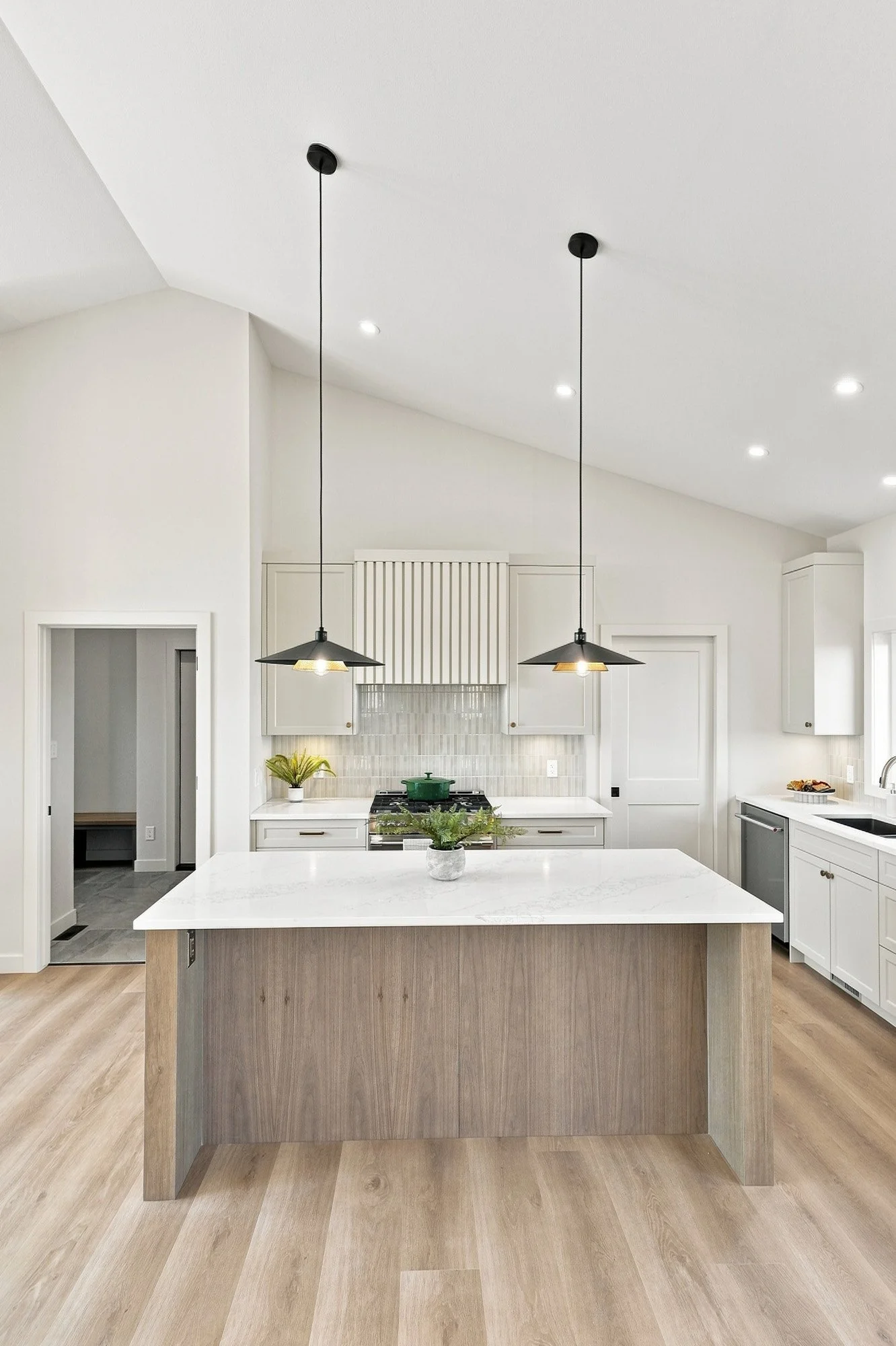 Modern kitchen with a marble island, wood floors, white cabinets, pendant lights, and a tile backsplash.