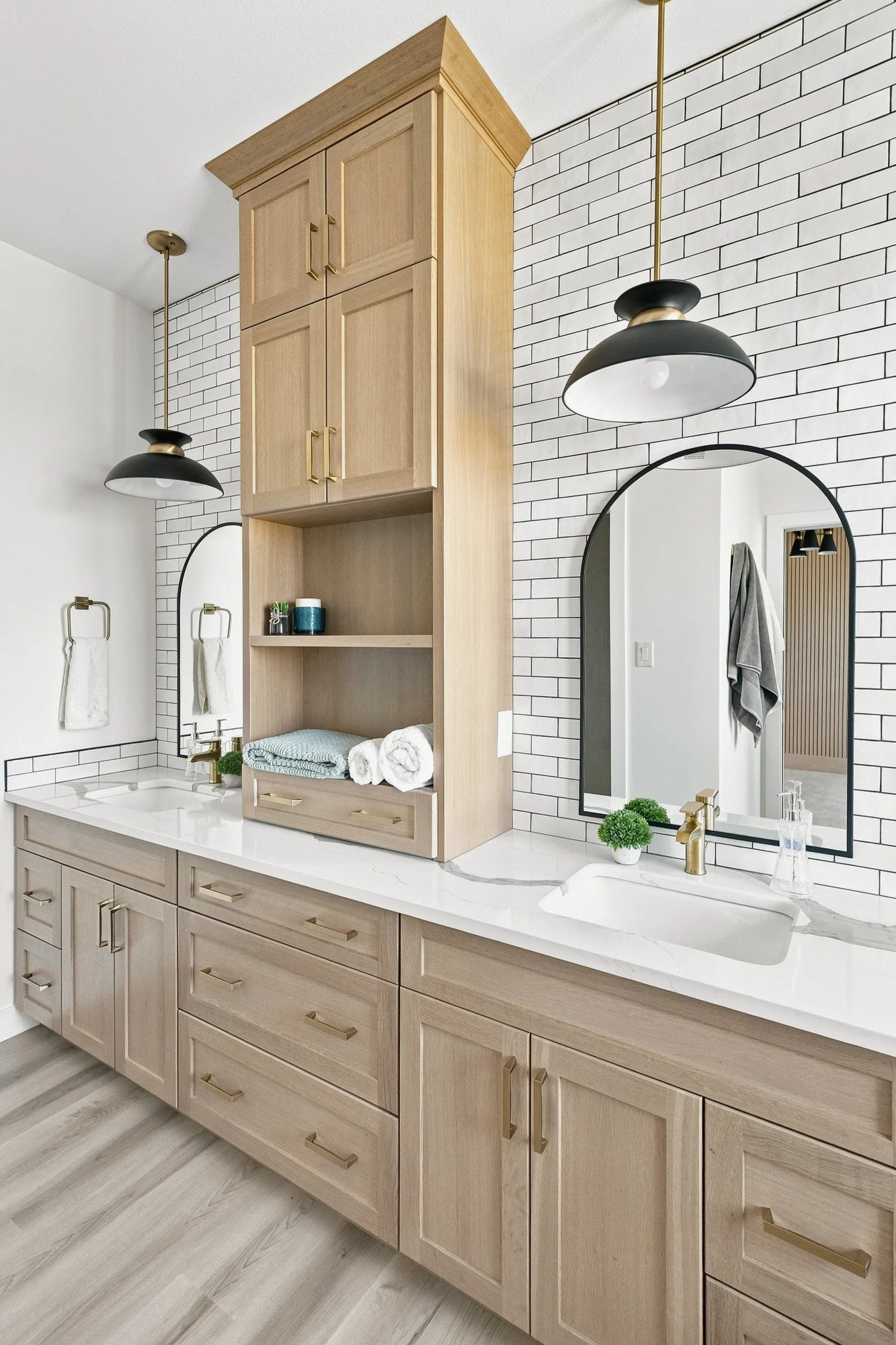 Modern bathroom with double sinks, wood cabinets, round mirrors, white tile backsplash, and gold fixtures.