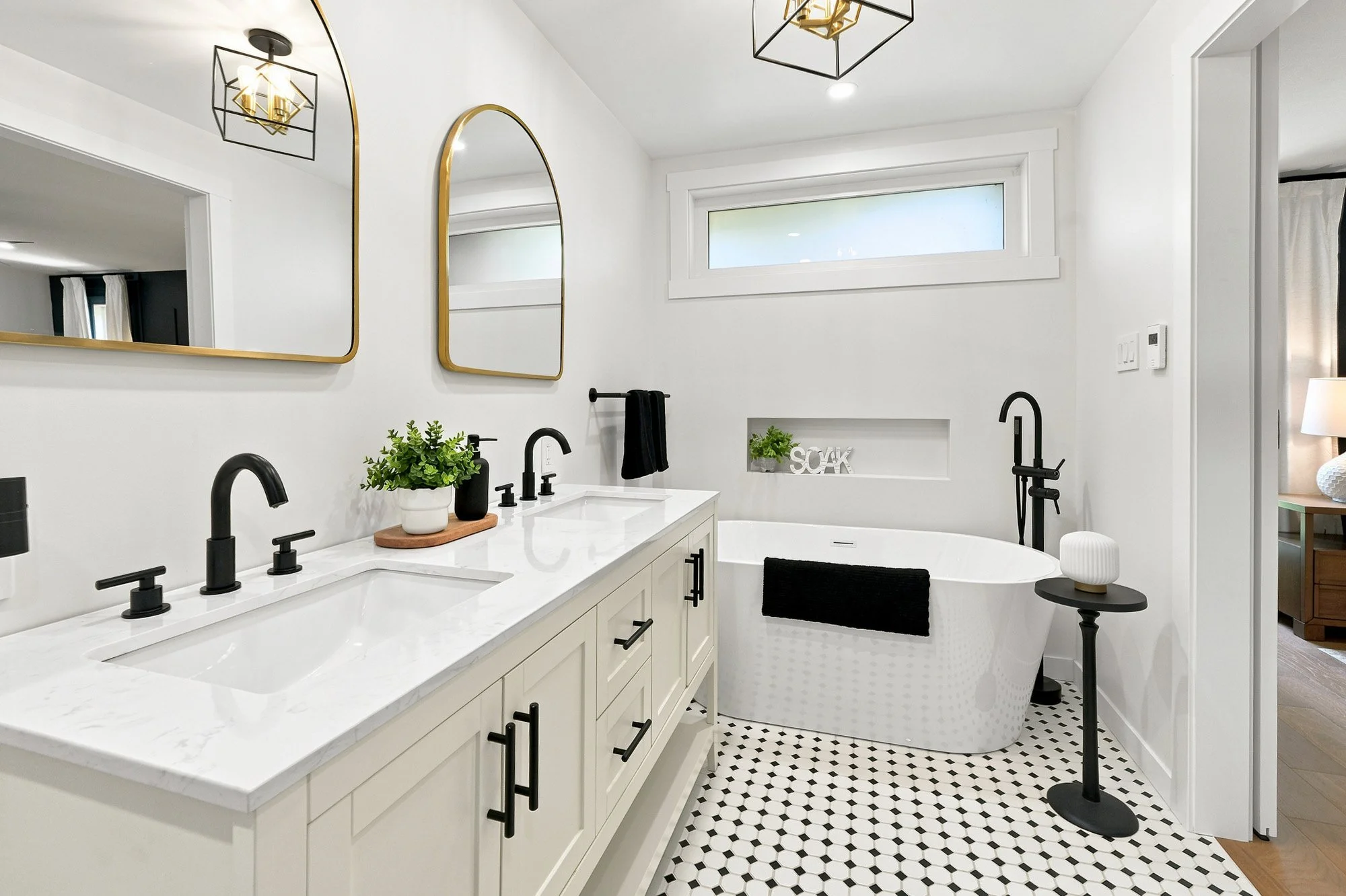 Luxury white bathroom with dual vanities, black fixtures, patterned flooring and a freestanding bathtub