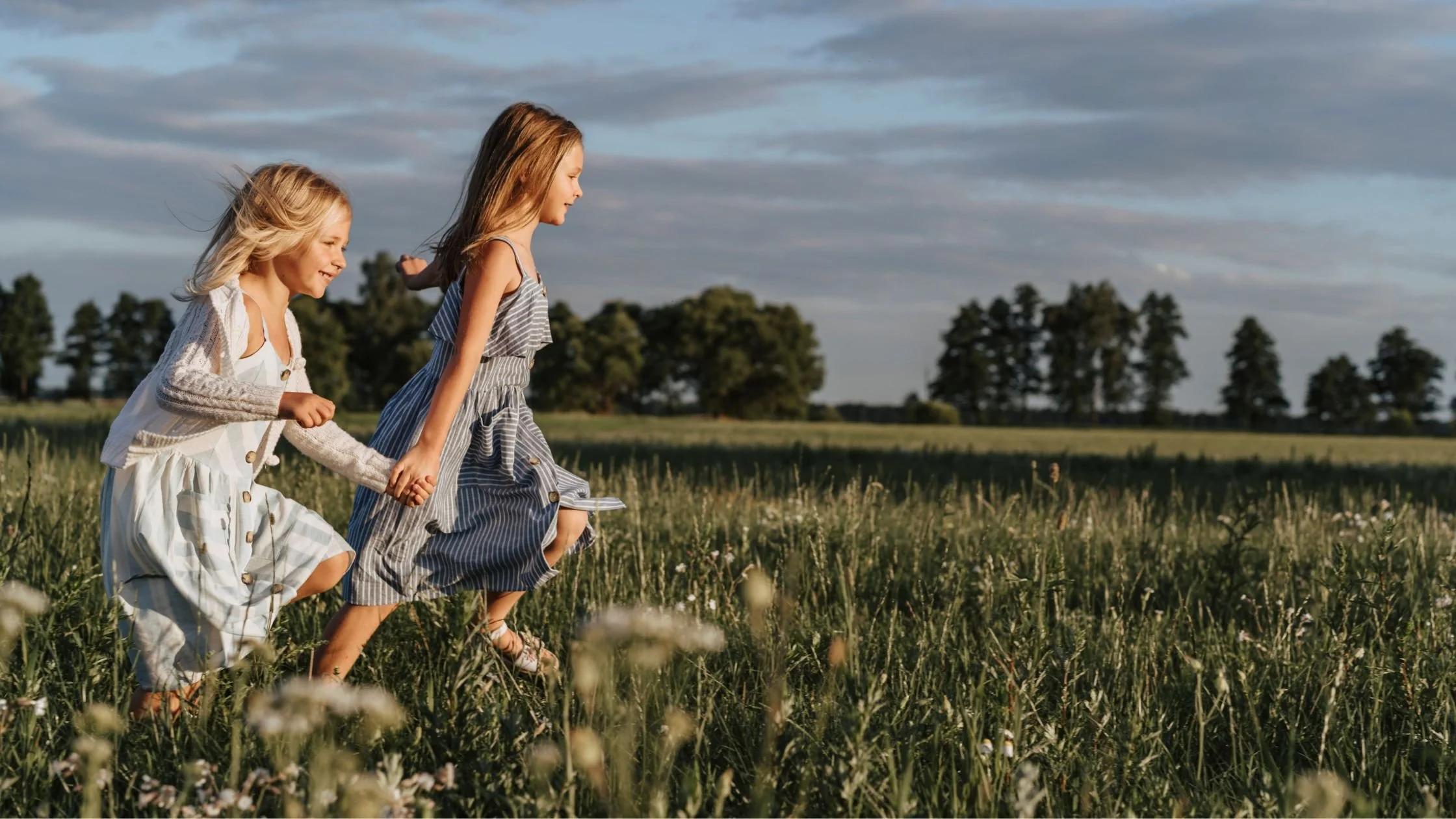 Two girls running through a field holding hands