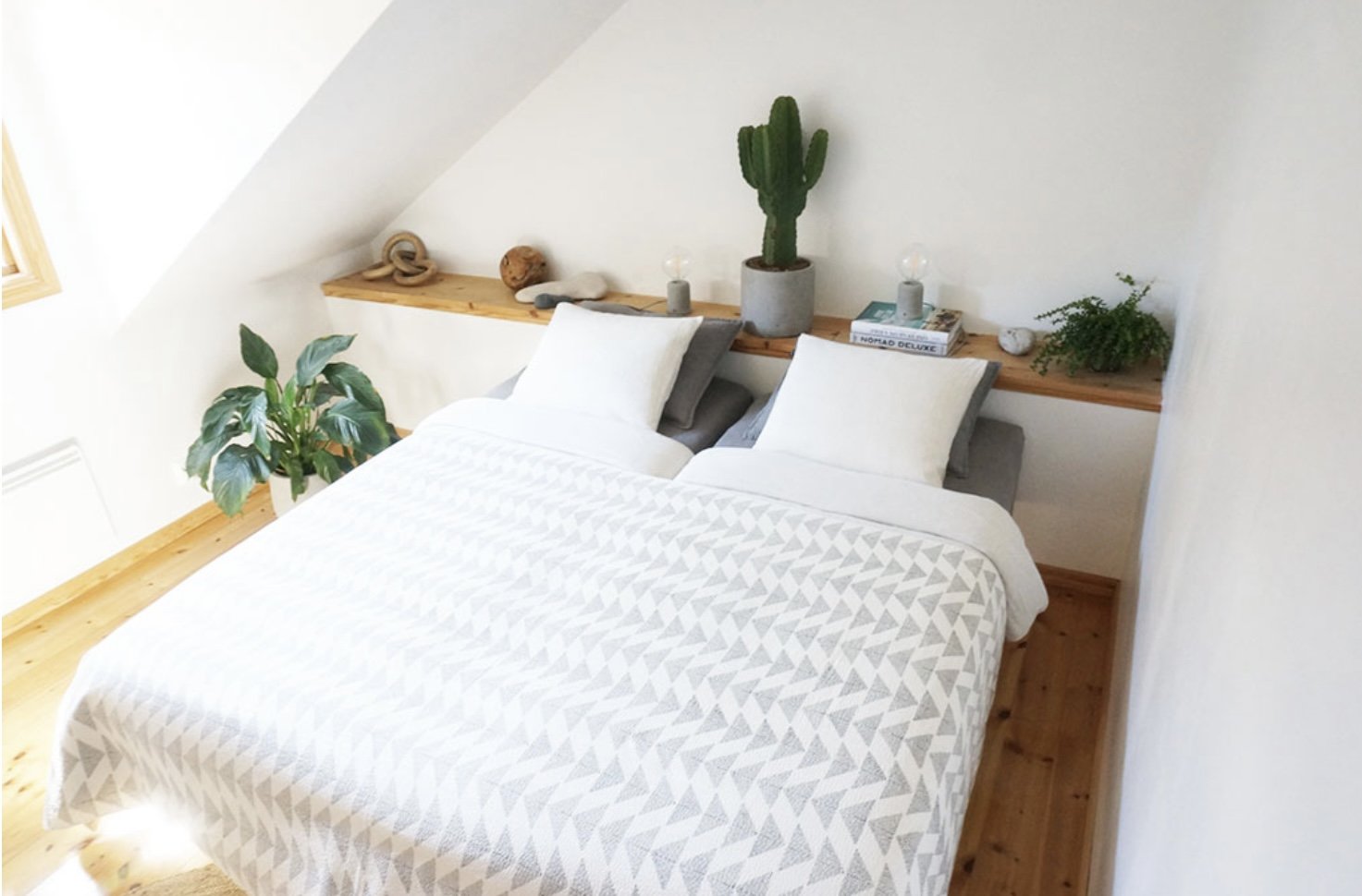Minimalist bedroom with white bedding, wooden floor, and decorative plants on a shelf.