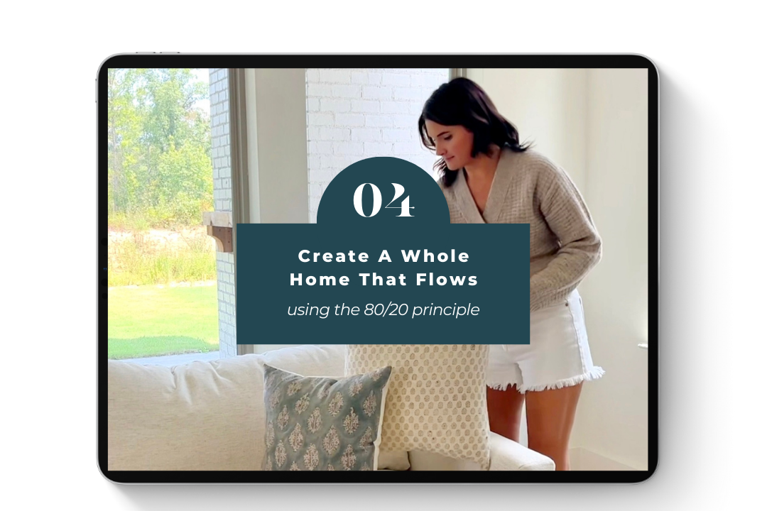 A woman adjusting pillows on a cream-colored sofa in a bright room with a large window showing greenery outside.