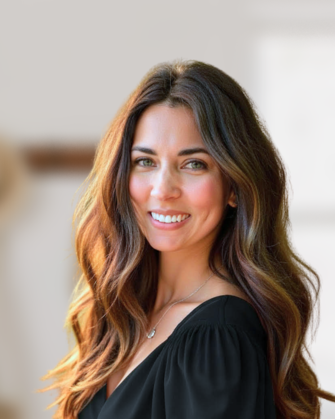 A woman with long wavy brown hair and green eyes, smiling and wearing a black top.