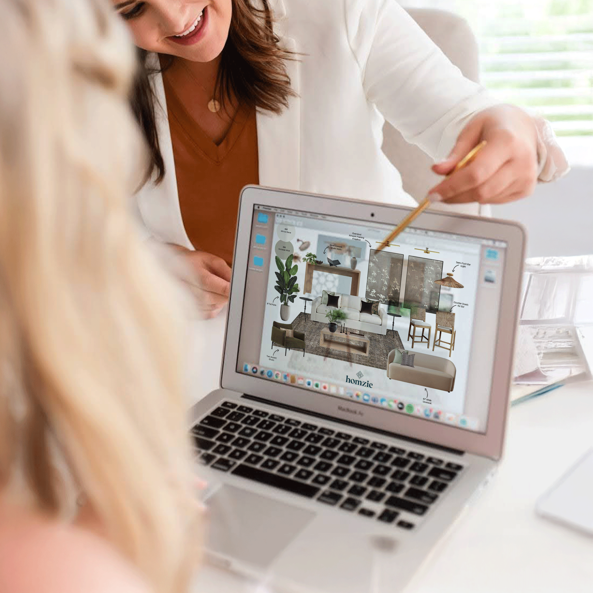 Woman showing a design plan on a laptop screen to another person, with sketches of a living room decor and furnishings.