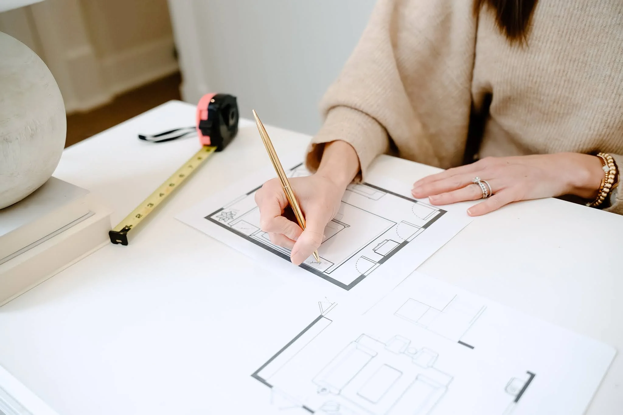 Person drawing floor plan on paper with architectural measurements on table.
