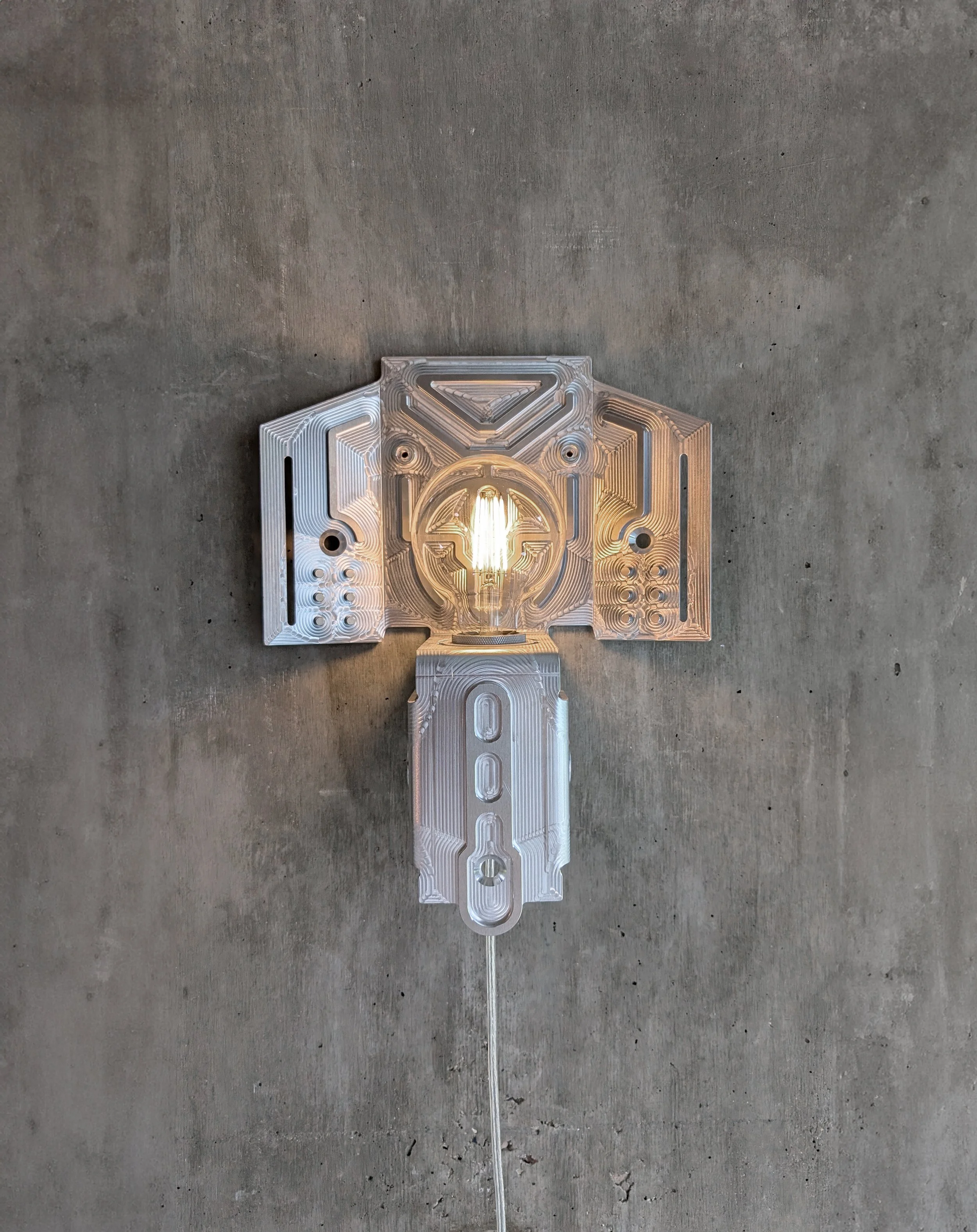 A modern wall-mounted lamp with a geometric metallic design, emitting a warm glow, mounted on a concrete wall.