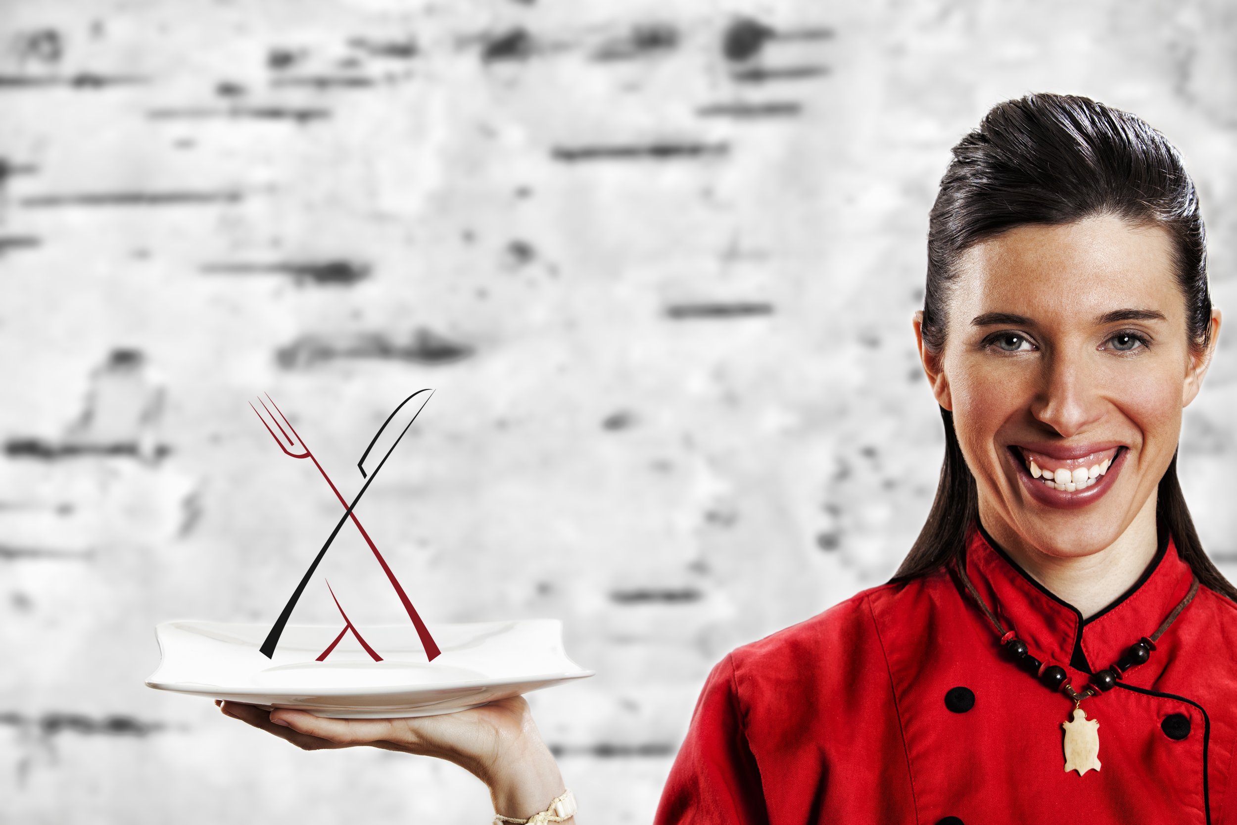 Une femme en uniforme rouge de chef cuisinier, souriante, tenant une assiette blanche avec des fourchettes et un couteau en métal stylisés plantés en croix