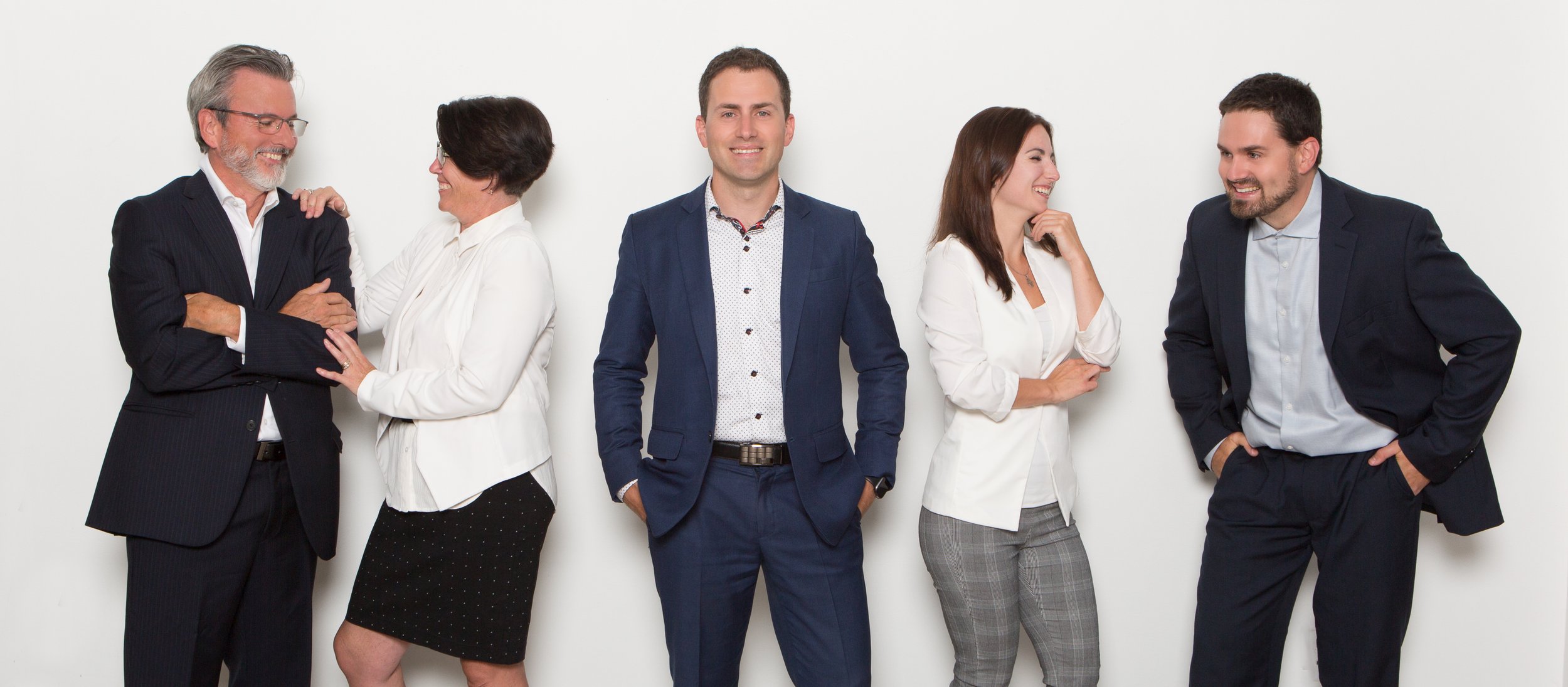 Photo d'équipe de travail - Groupe de cinq personnes habillées en tenue professionnelle, posant et souriant devant un fond blanc.