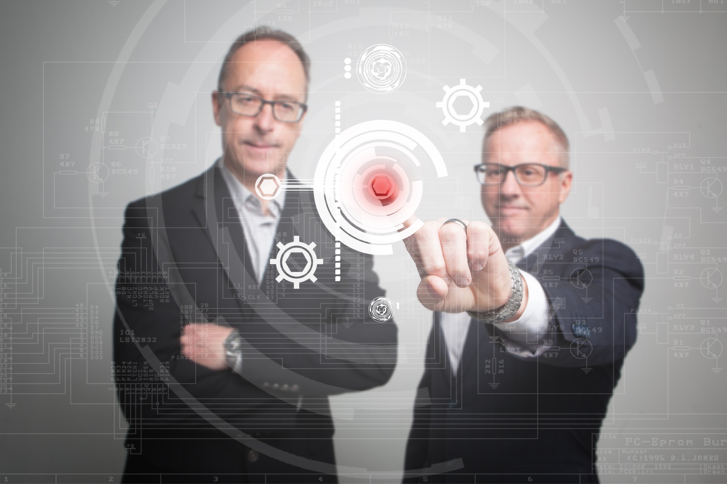 Portrait d'affaires - Deux hommes d'affaires en costume interagissent avec une interface technologique futuriste contenant des diagrammes et des icônes numériques.