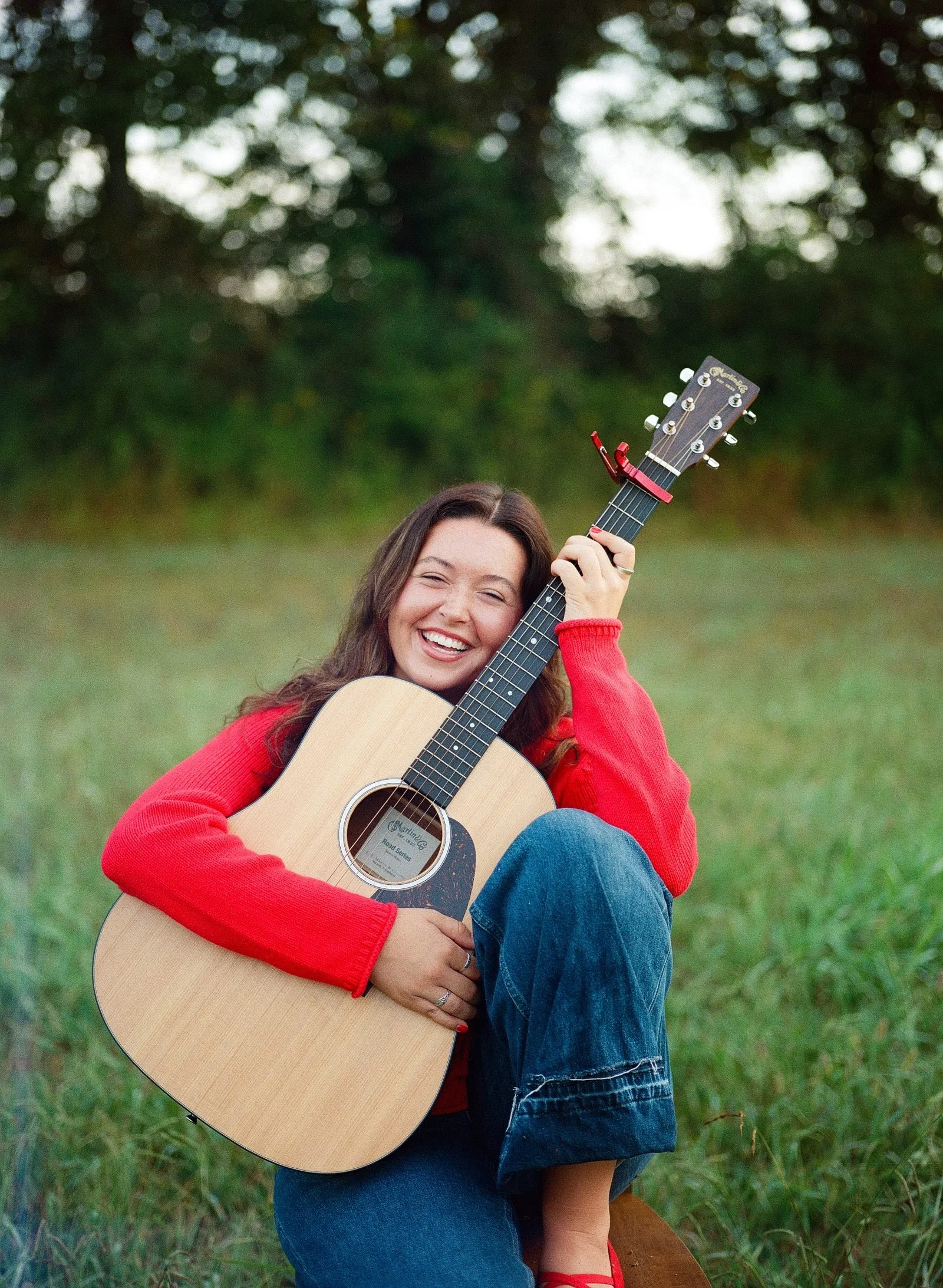 Katie Flemming laughing with her acoustic guitar in a field