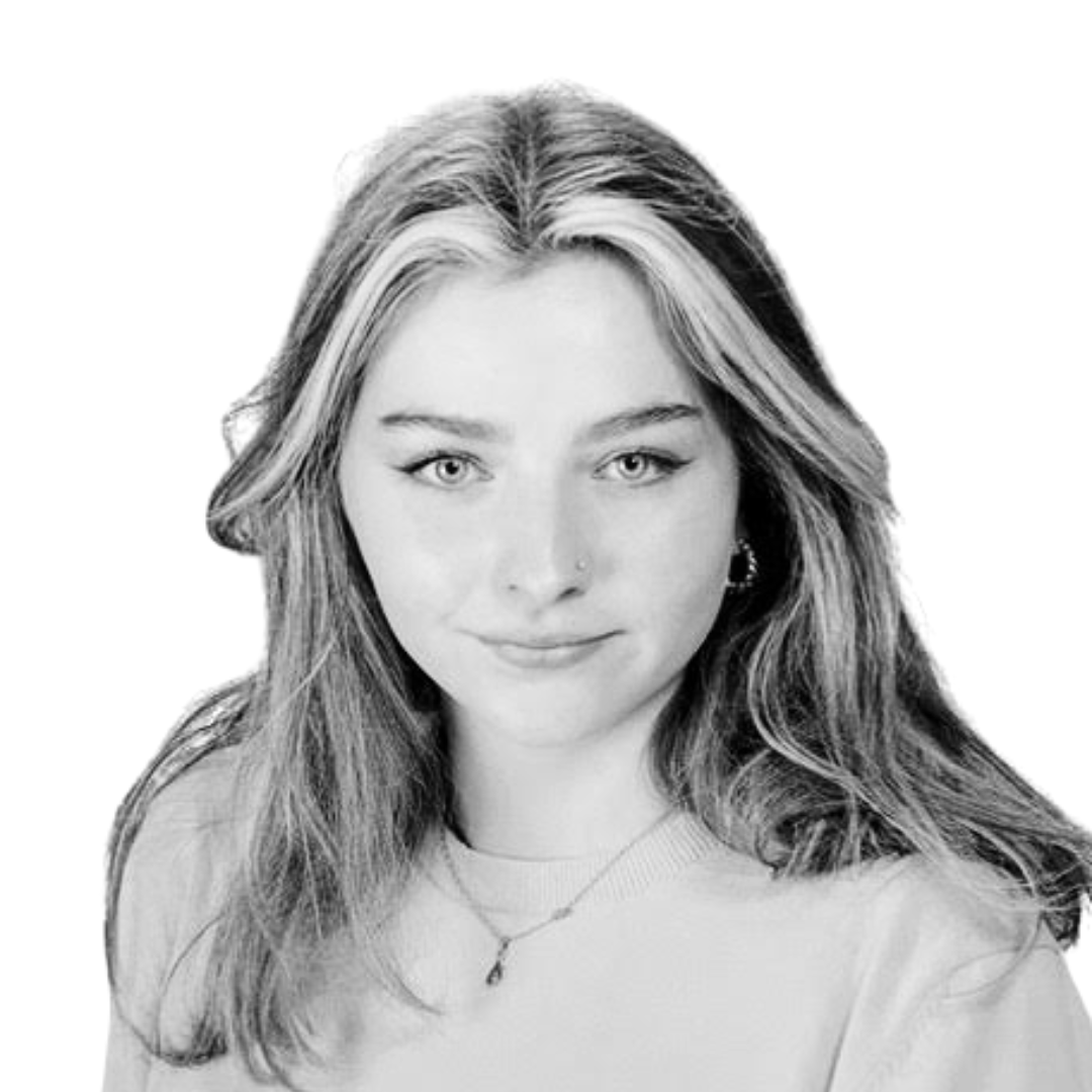 Black and white close-up portrait of a young woman with wavy hair, a nose ring, and a necklace, against a plain light background.