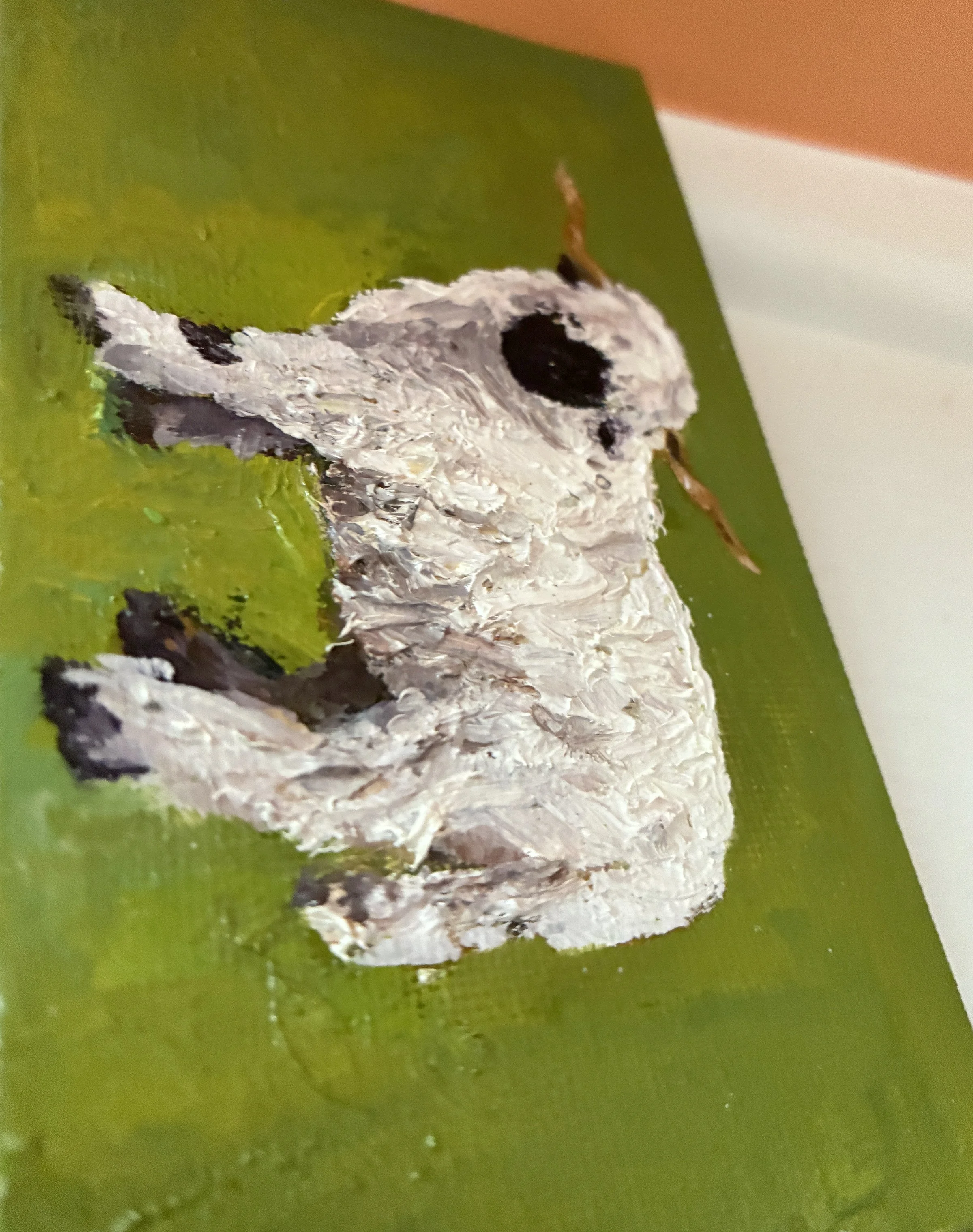 Detail of an oil painting of a white sheep with a black face and hooves on an abstract green background. The photo shows the texture of the of the painting.