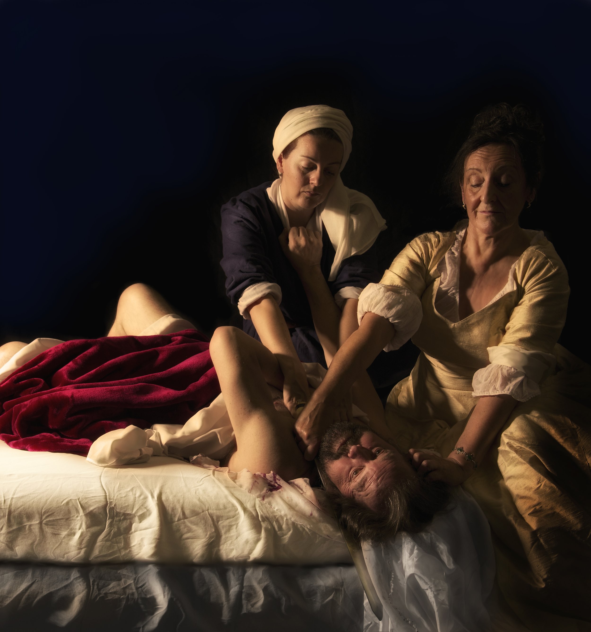 Two ladies cutting the throat of the man on the table