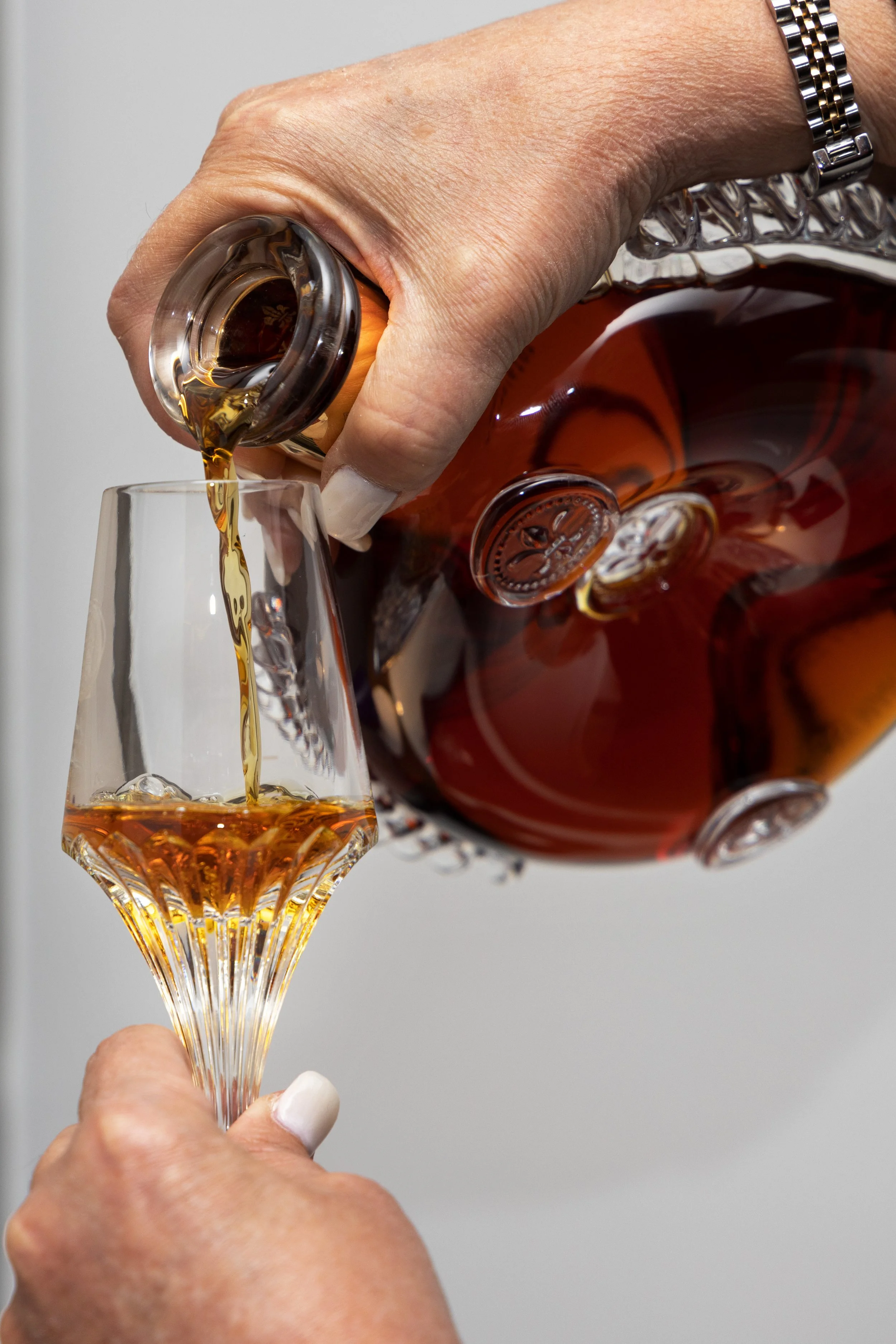 A person pours whiskey from a glass decanter into a crystal glass.