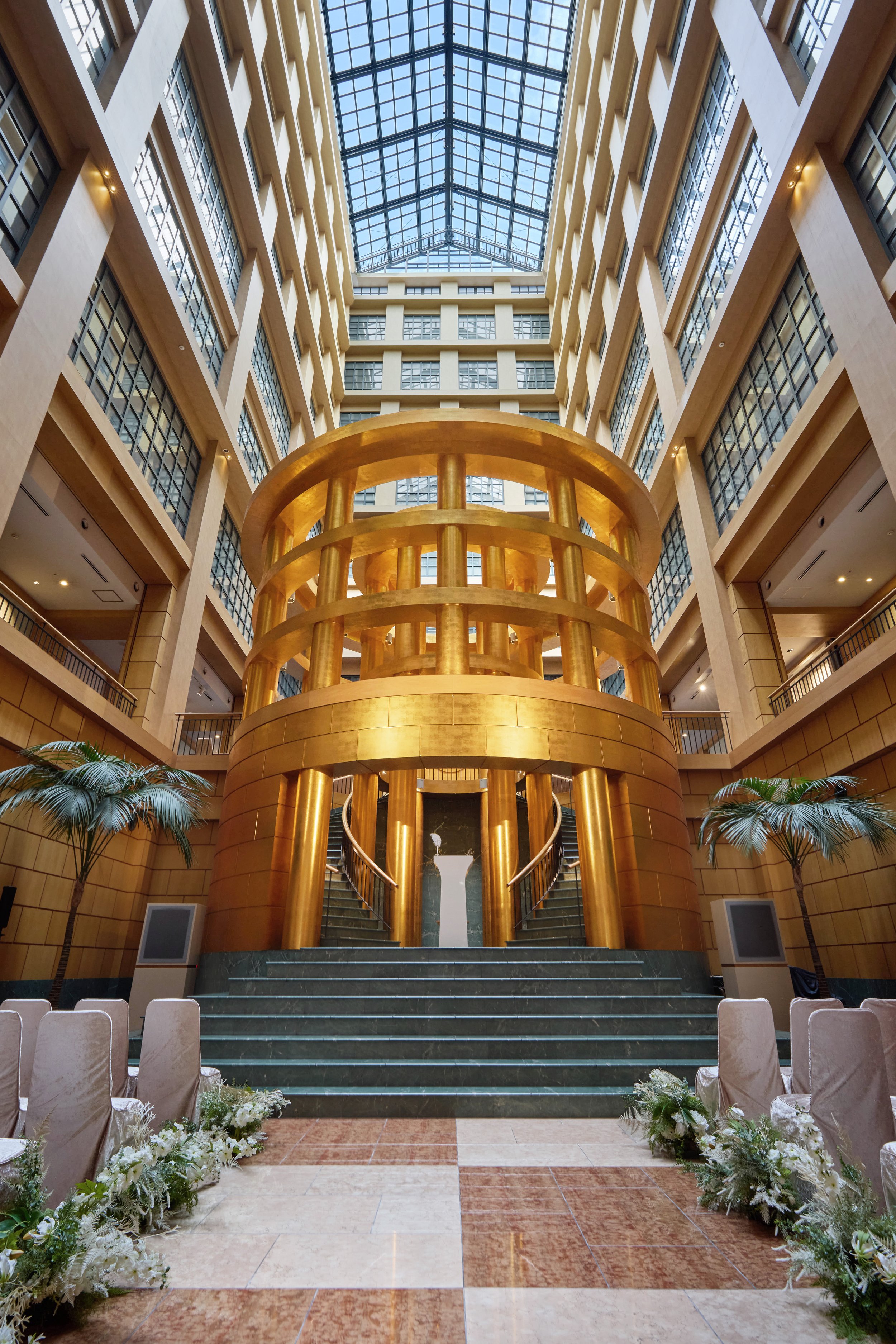 Atrium wedding ceremony setup beneath the central rotunda at The Basics Fukuoka, highlighting the scale, symmetry, and architectural drama of the hotel’s interior gathering space.