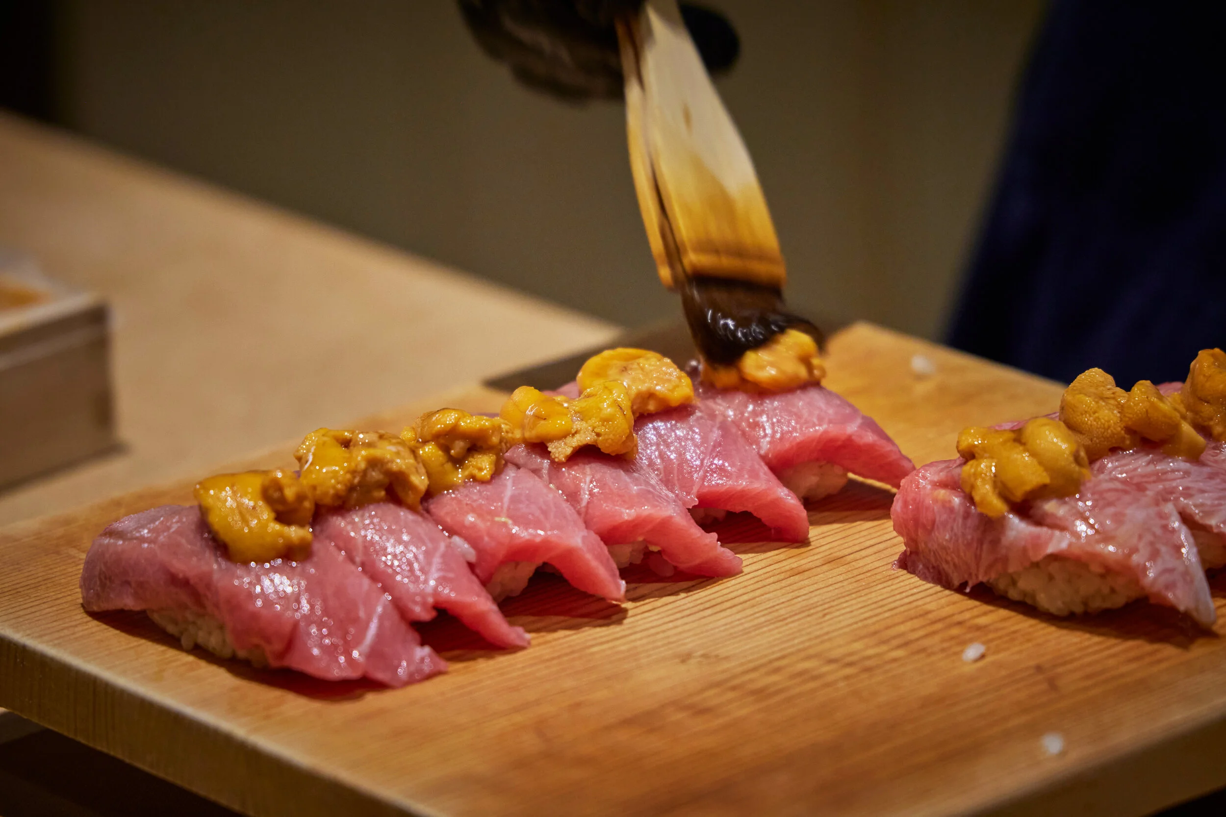 Sushi being topped with sea urchin from a brush by a chef's hand.
