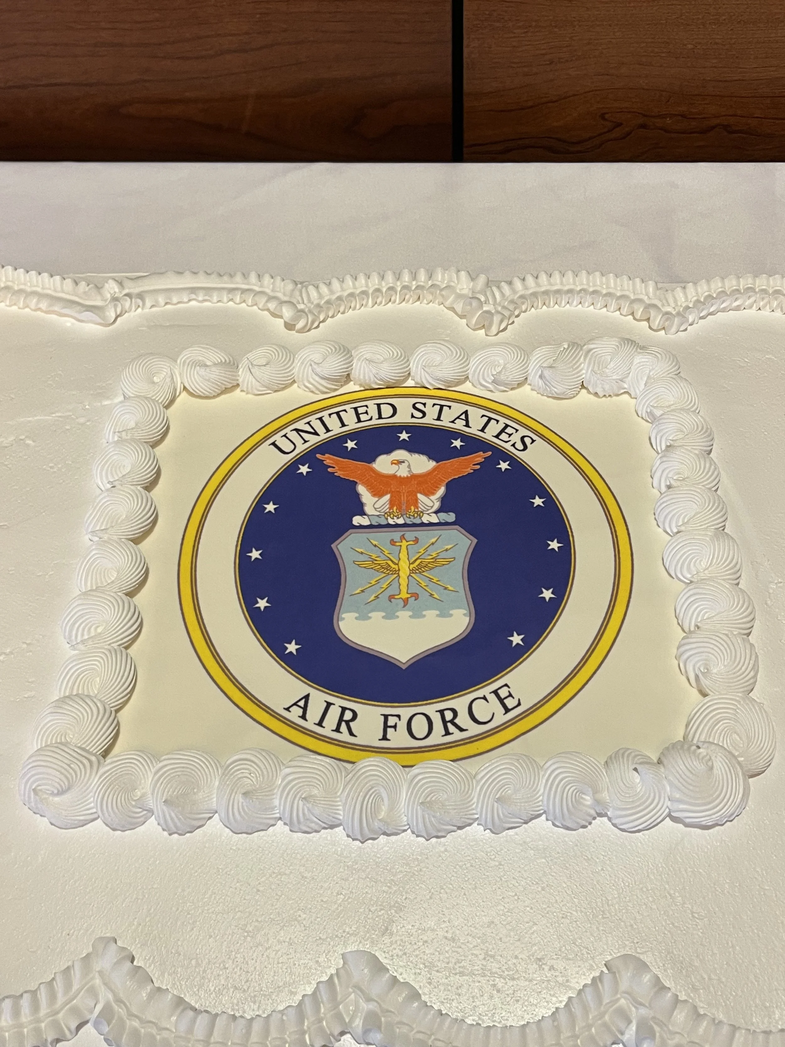 Cake decorated with the emblem of the United States Air Force on top, surrounded by white frosting with piped borders.