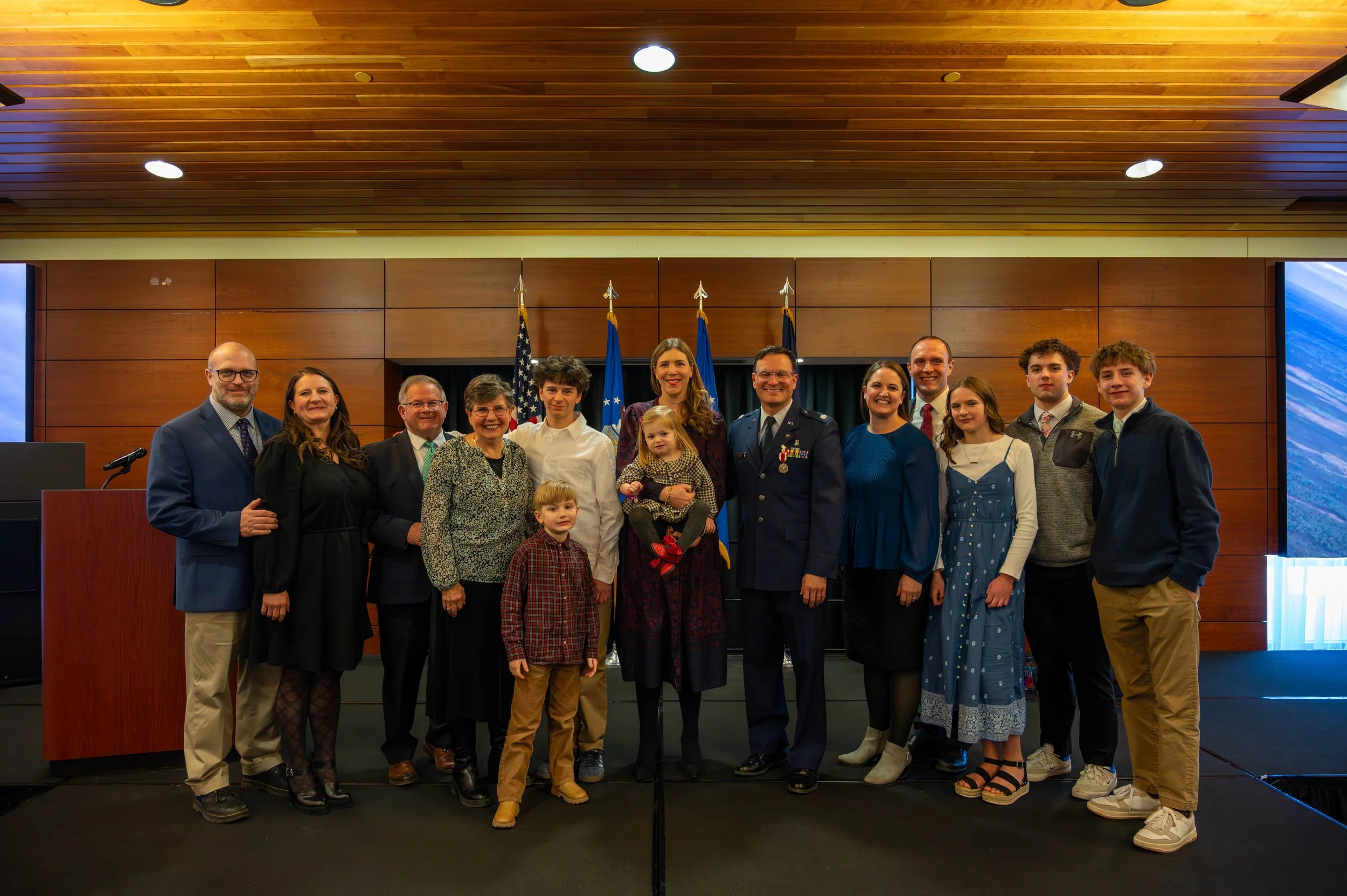 Group of people posing together in a formal setting with flags in the background.