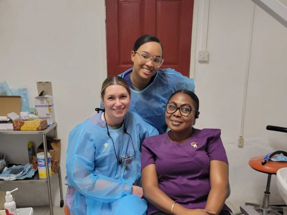 Three women in medical scrubs smiling and posing for a photo in a clinic or hospital setting.