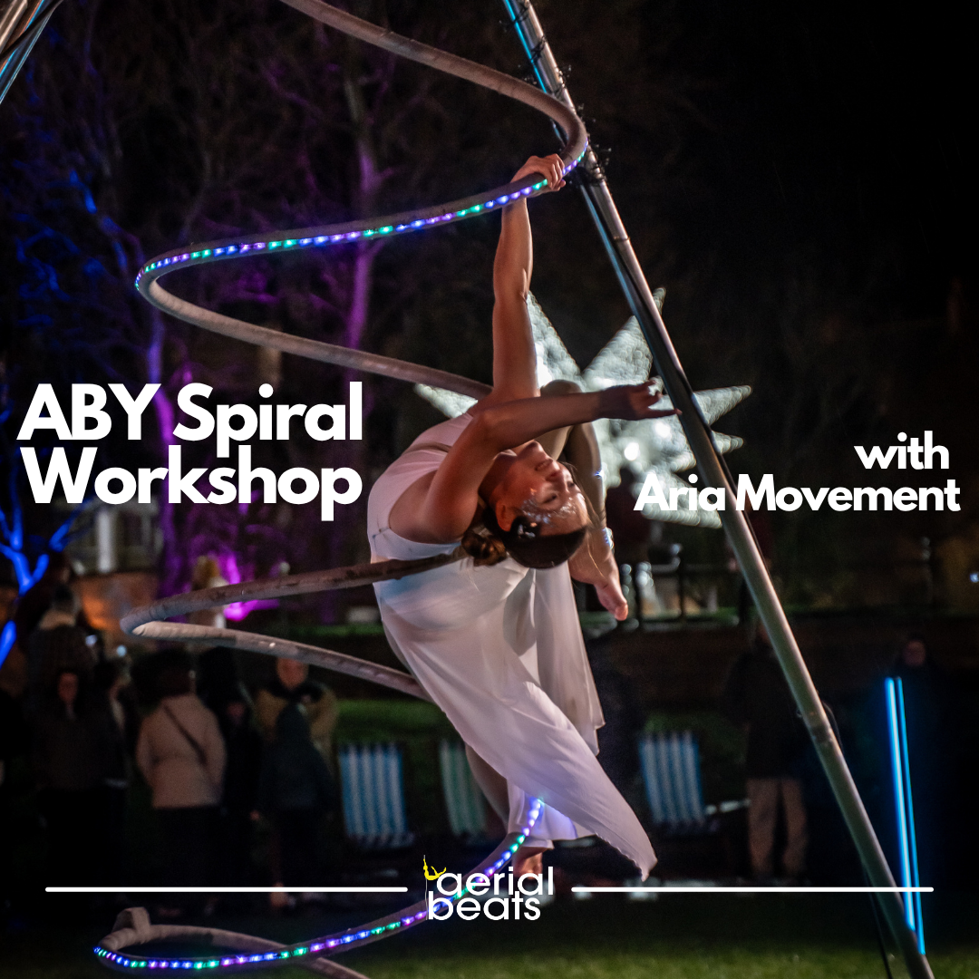 A performer spinning in a large metal hoop decorated with colorful LED lights at night, part of a circus or acrobatic performance.