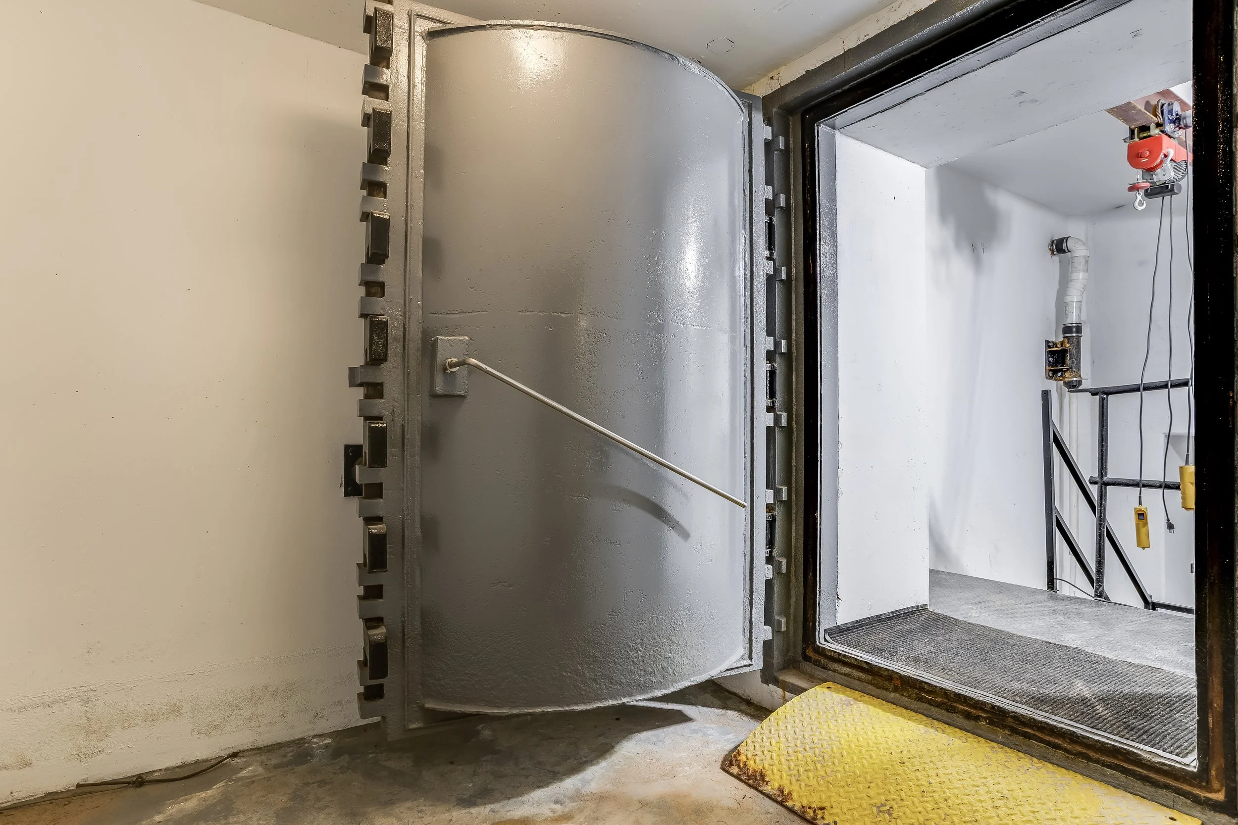 An elevator door is open, revealing a metal elevator shaft and a yellow safety mat on the floor outside the elevator.