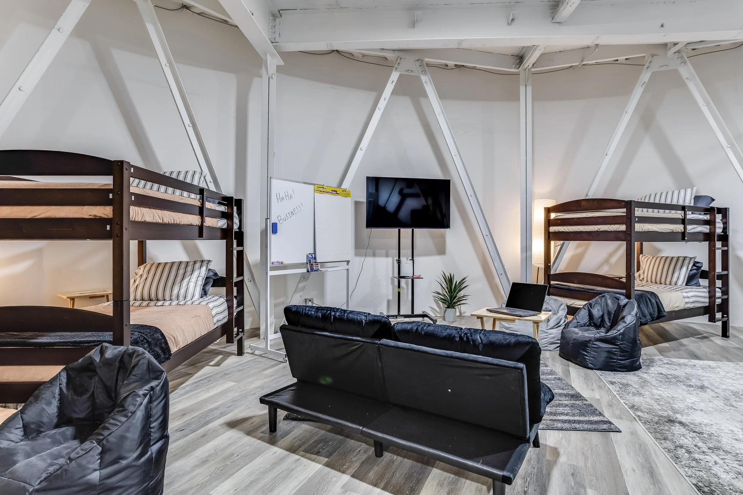 Bunkroom with multiple bunk beds, lounge seating, and exposed A-frame silo beams, sleeping large groups in the underground bunker.