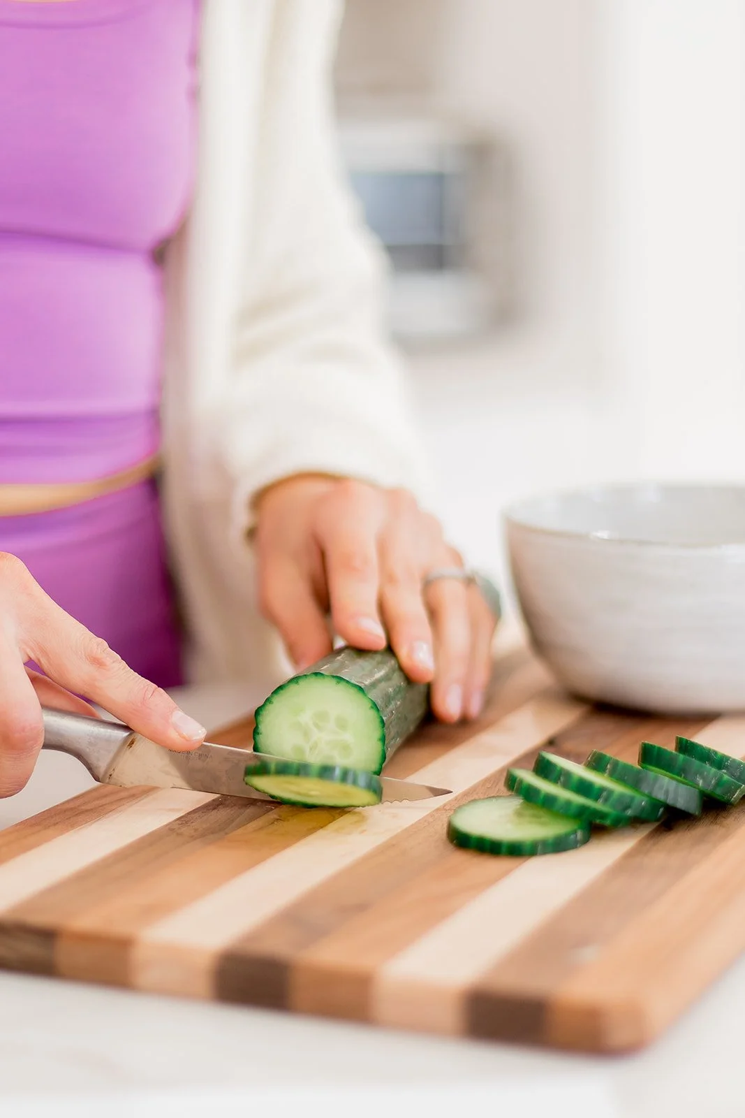 Person slicing cucumber on a wooden cutting board in a kitchen.