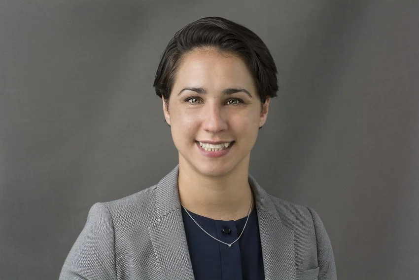 Professional portrait of Jen wearing a gray blazer against a gray background